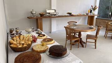 Un bufé de desayuno con diversos pasteles, tortas y bebidas sobre una mesa con sillas de madera.