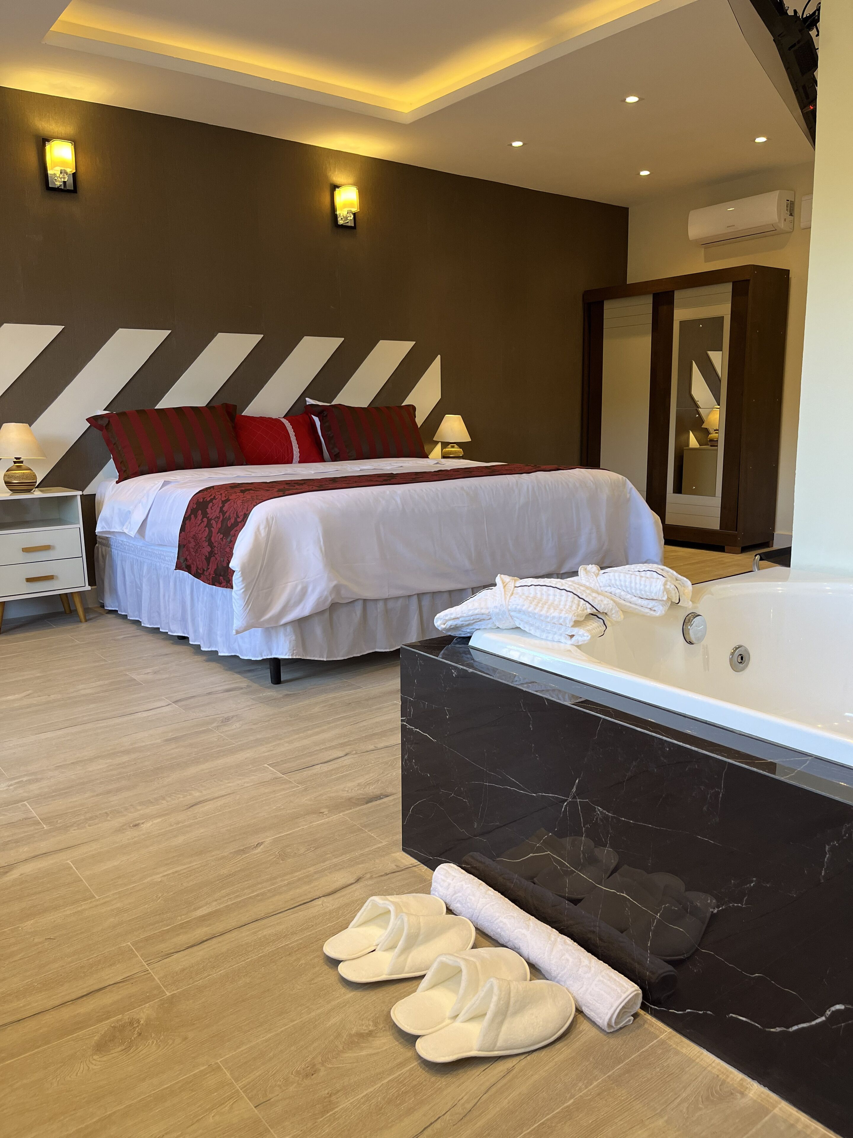 Una habitación de hotel moderna con una cama grande, una zona de estar separada, un baño con bañera y suelo de madera.