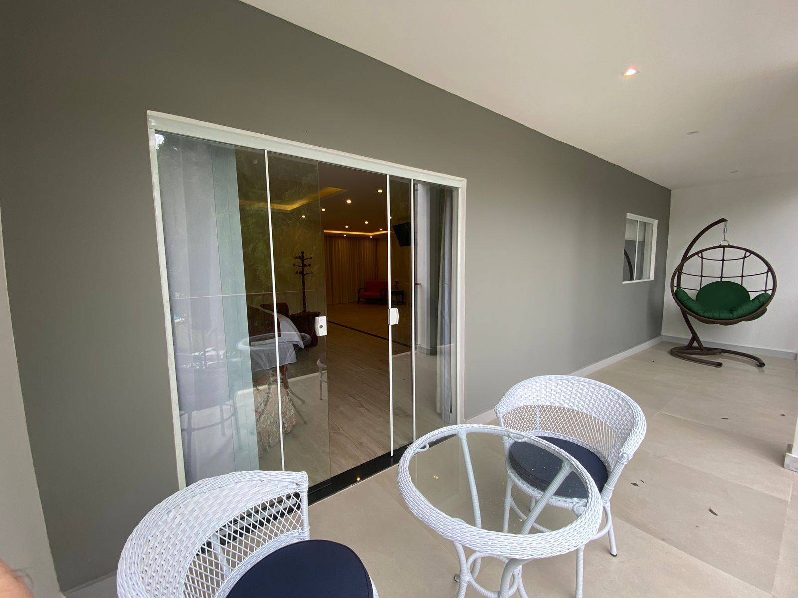 Un interno moderno con una porta vetrata che dà su un'area living, due poltrone in vimini bianco e una sedia sospesa.