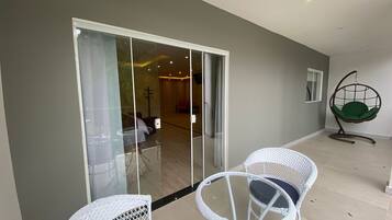 A modern interior with a glass door leading to a living area, two white wicker chairs, and a hanging chair.