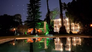 Vista nocturna de un hotel con una piscina que refleja el edificio y los árboles.