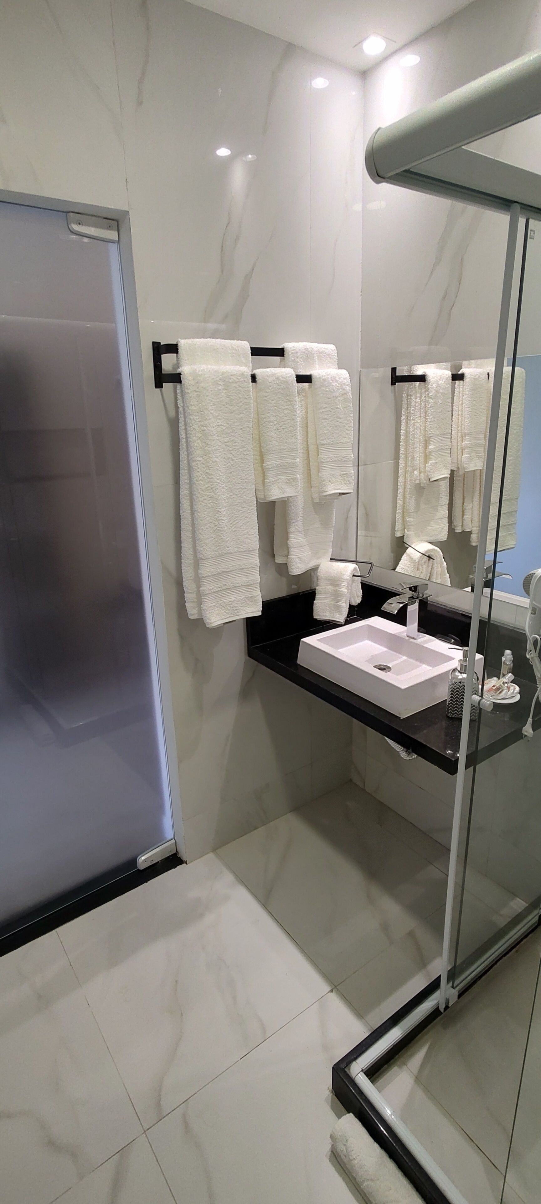 A modern bathroom with a glass shower enclosure, a black countertop sink, and multiple white towels hanging on a rack.