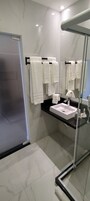 A modern bathroom with a glass shower enclosure, a black countertop sink, and multiple white towels hanging on a rack.