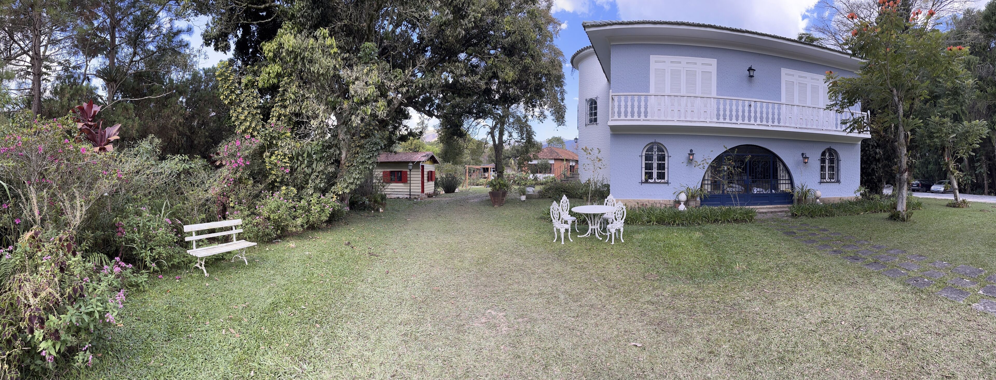 A white building with a balcony, surrounded by lush greenery and a grassy lawn.