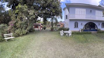 A white building with a balcony, surrounded by lush greenery and a grassy lawn.