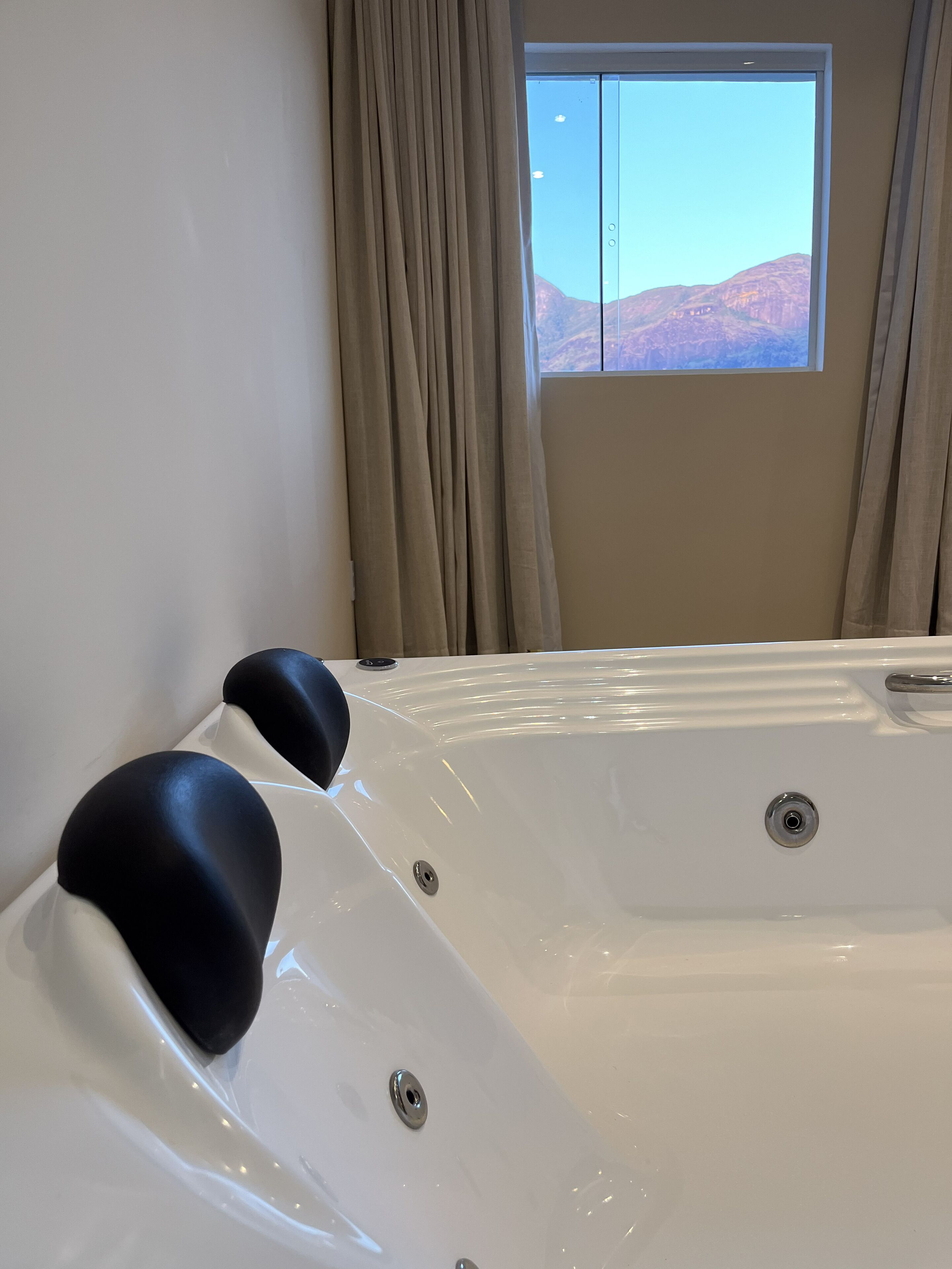 Une pièce avec une grande baignoire blanche, des rideaux beiges et une fenêtre donnant sur les montagnes.