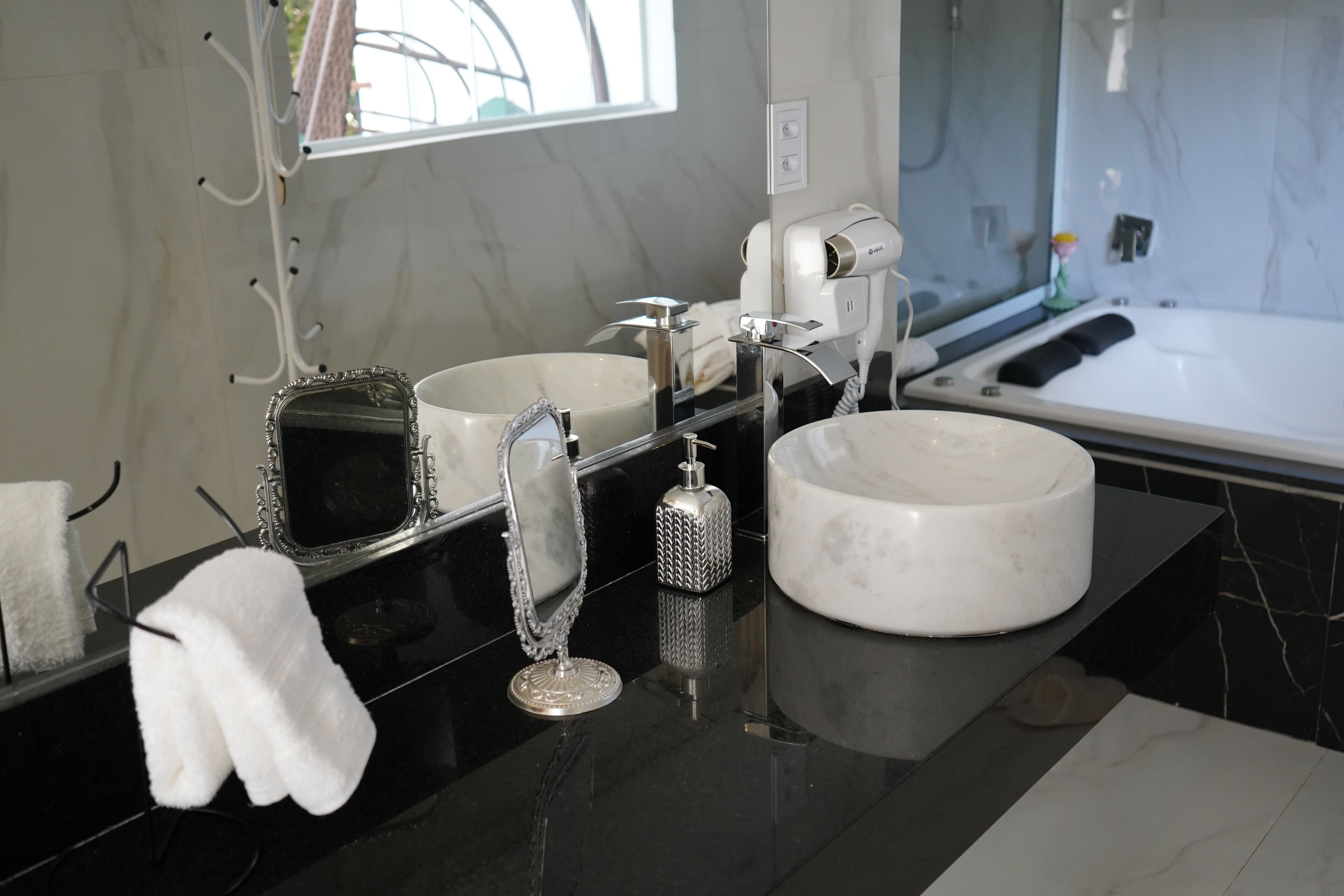 A modern bathroom with a large mirror, two sinks, a hairdryer, and a towel rack.
