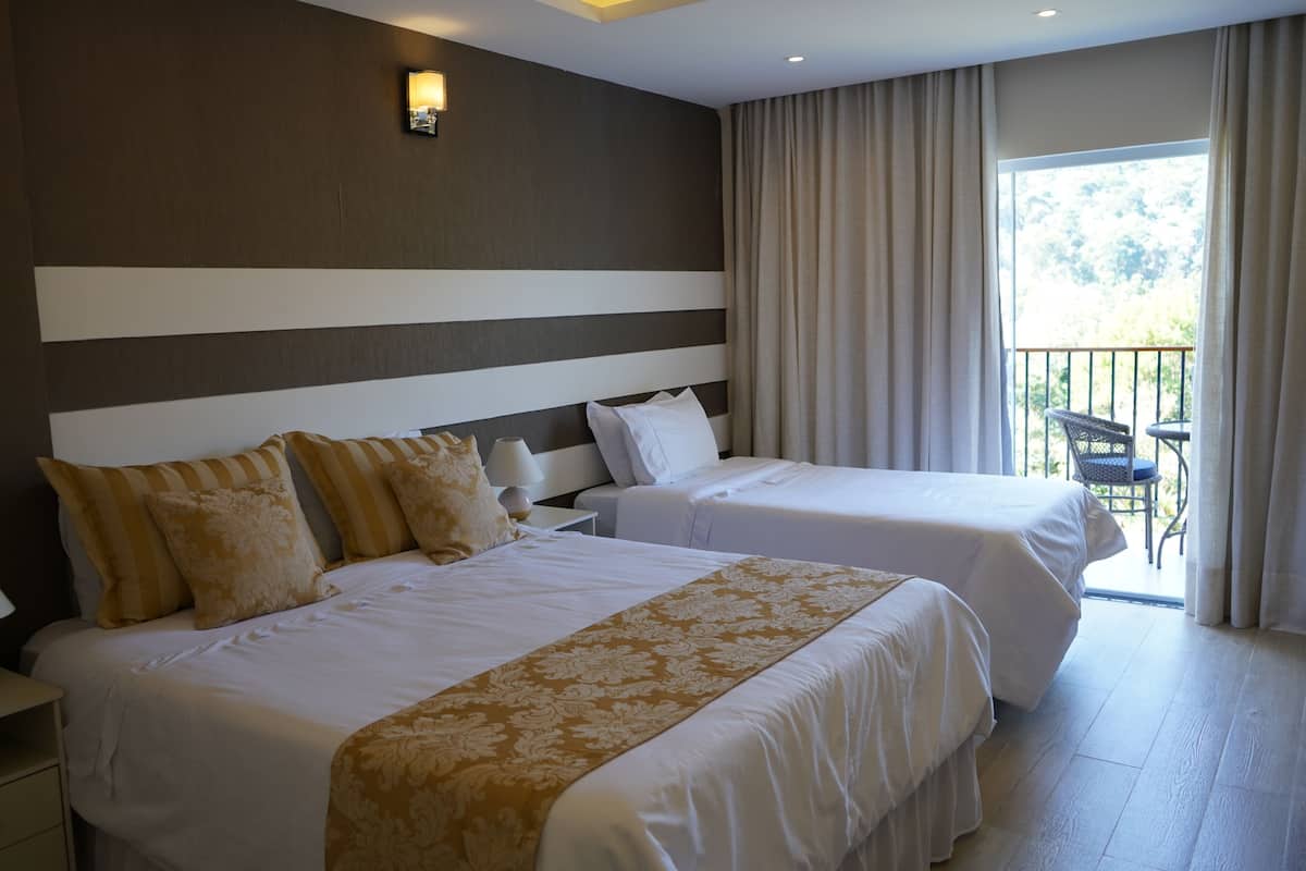 A hotel room with two beds, a nightstand, a lamp, and a balcony with a chair.