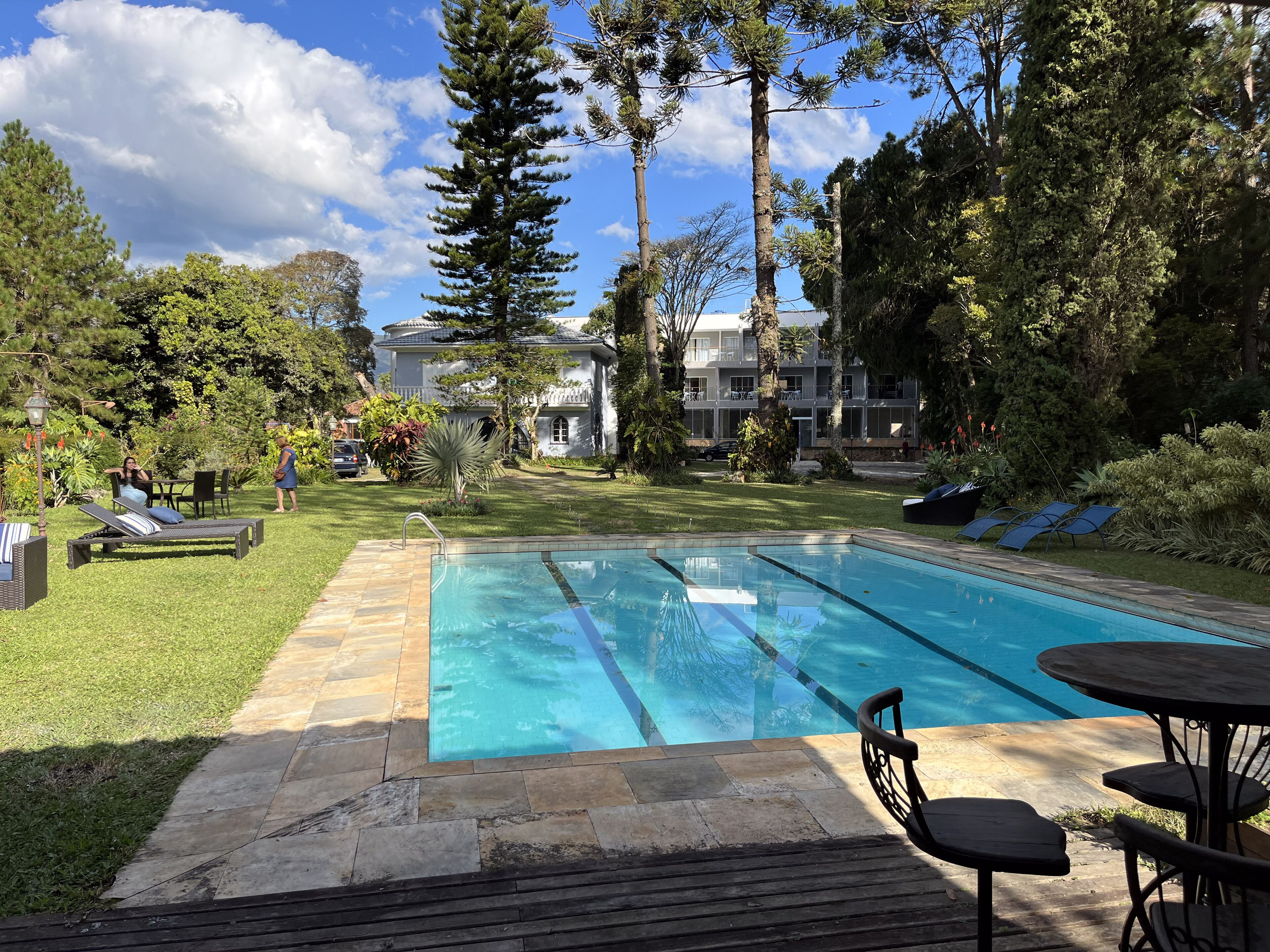 A swimming pool with a clear blue water, surrounded by a well-maintained lawn and trees. There are lounge chairs and a table near the pool.