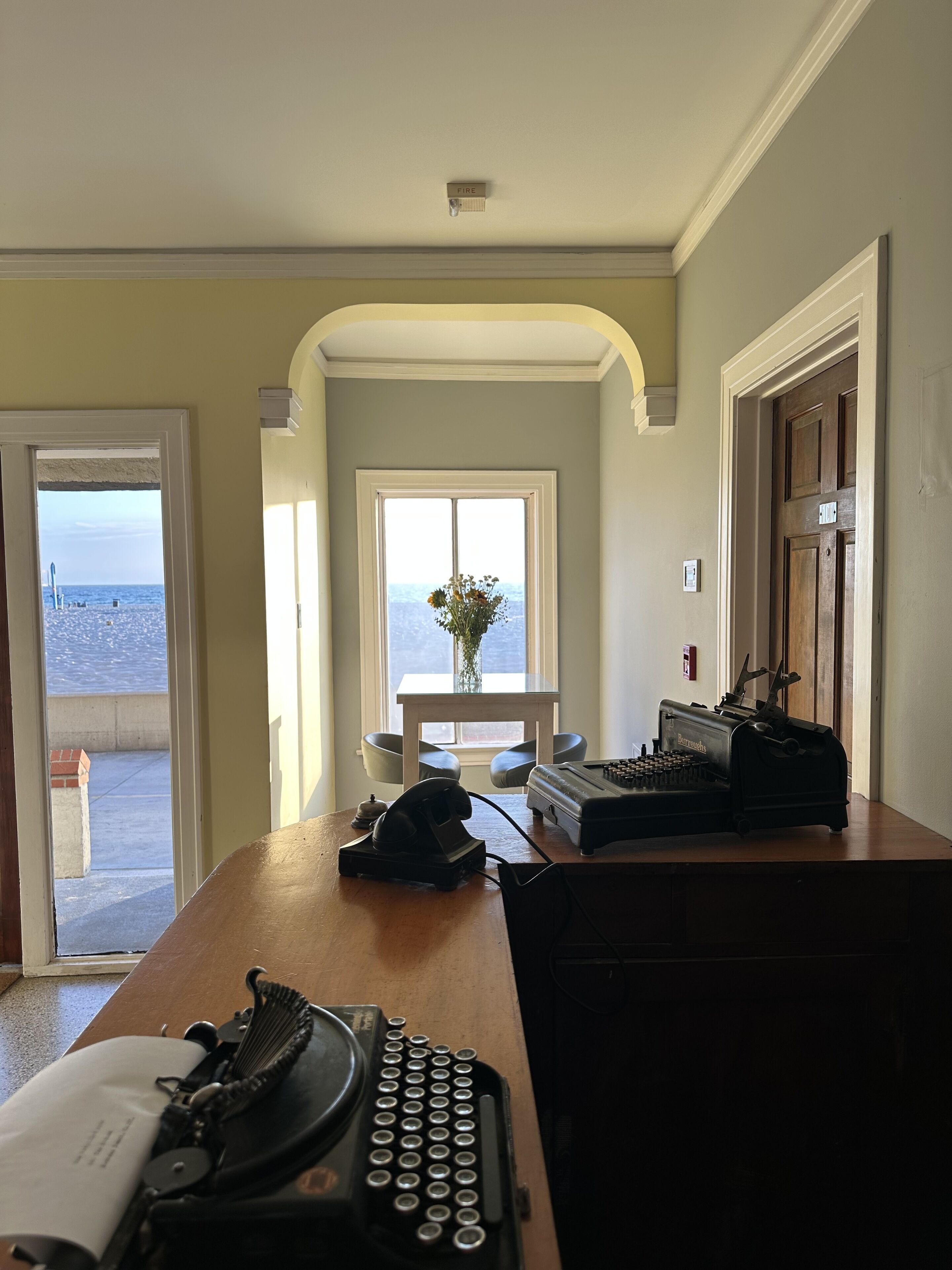 Una habitación con escritorio, máquina de escribir, teléfono y ventana con vista al mar.