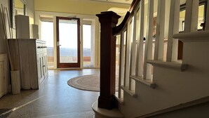 A spacious hallway with a wooden staircase, a large mirror, and a view through an open door to the outside. - The Vurpillat Beachfront Hotel (Hermosa Beach)