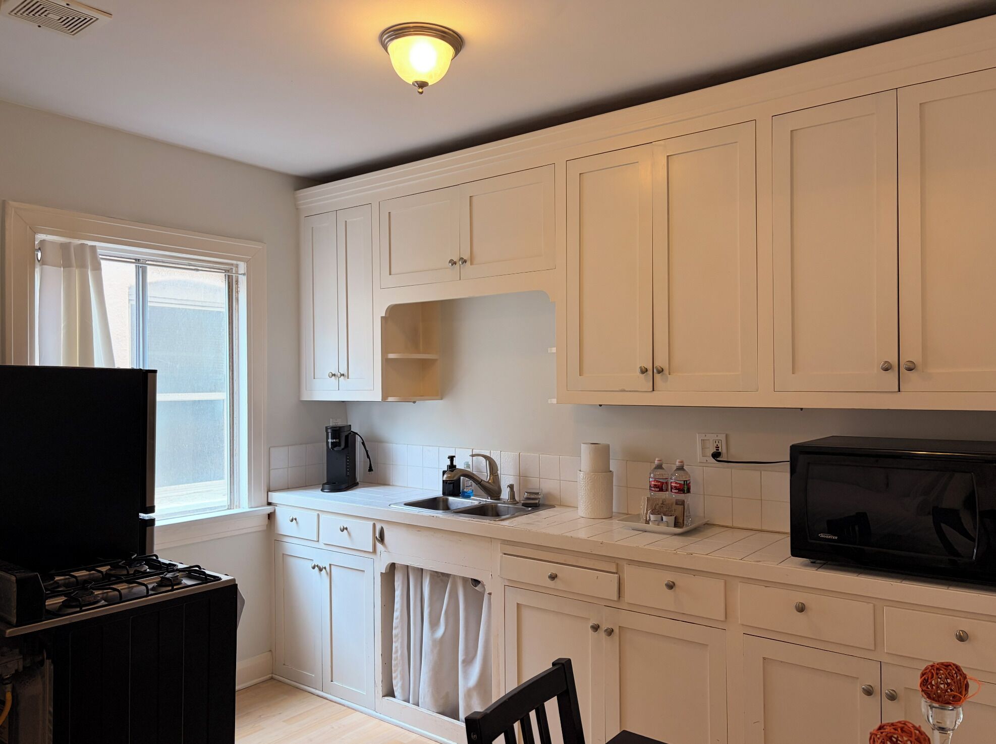 A kitchen with white cabinets, a stove, a microwave, and a window.