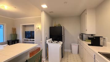 Una cocina compacta con armarios blancos, un refrigerador negro, una estufa a gas y un microondas.