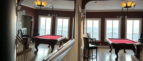 A pool room with two pool tables, a billiard rack, and a mirror reflecting the room.