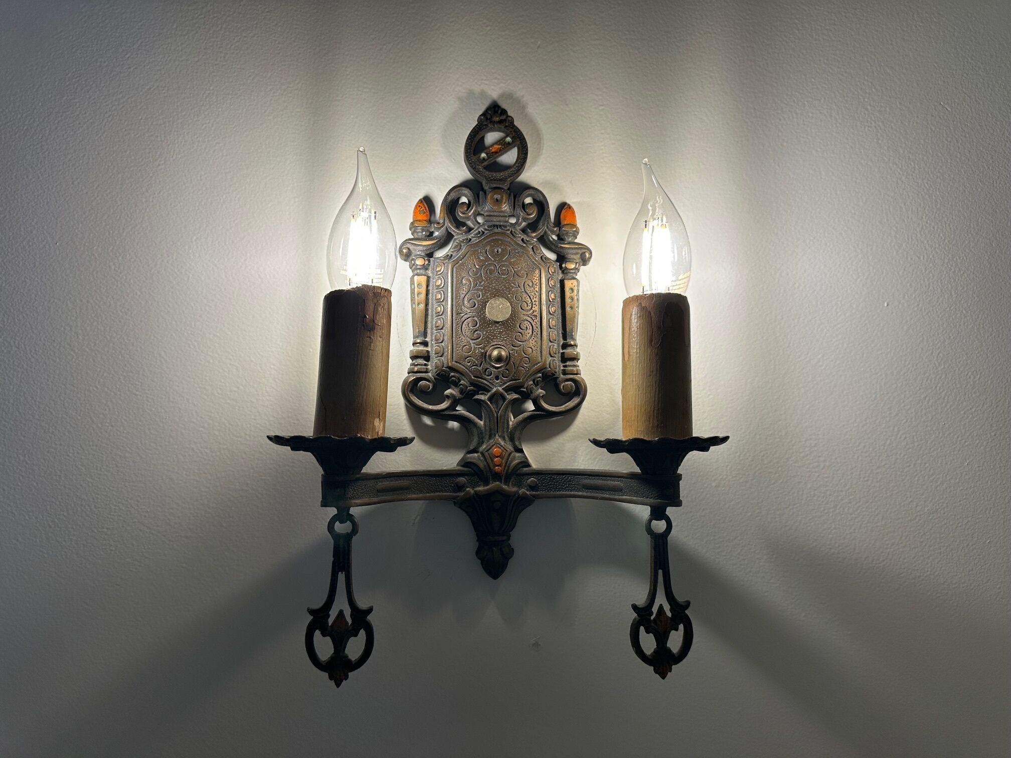 A wall-mounted light fixture with two candles and two glass bulbs.