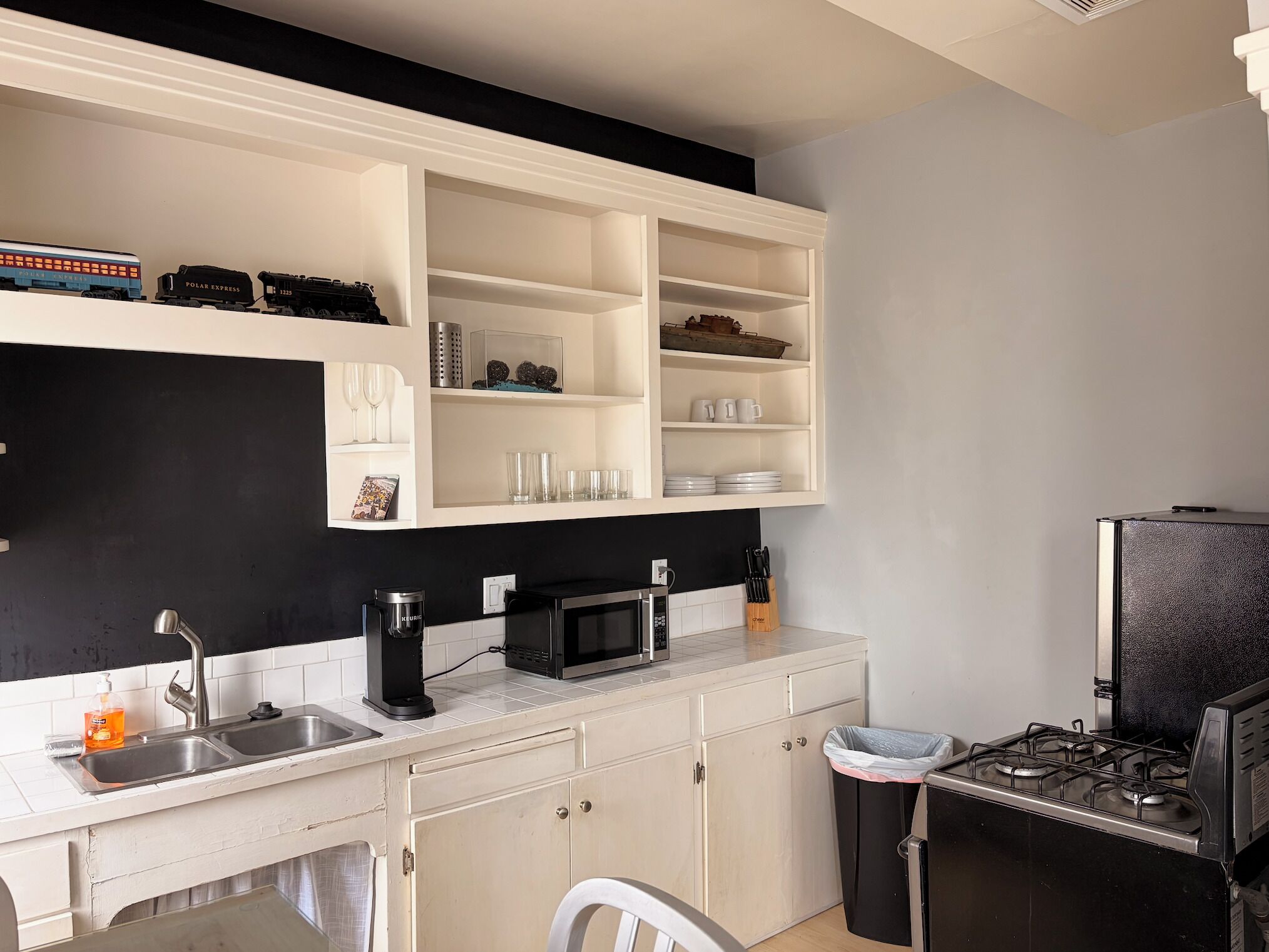A kitchen with a black countertop, white cabinets, a microwave, a sink, and a stove.