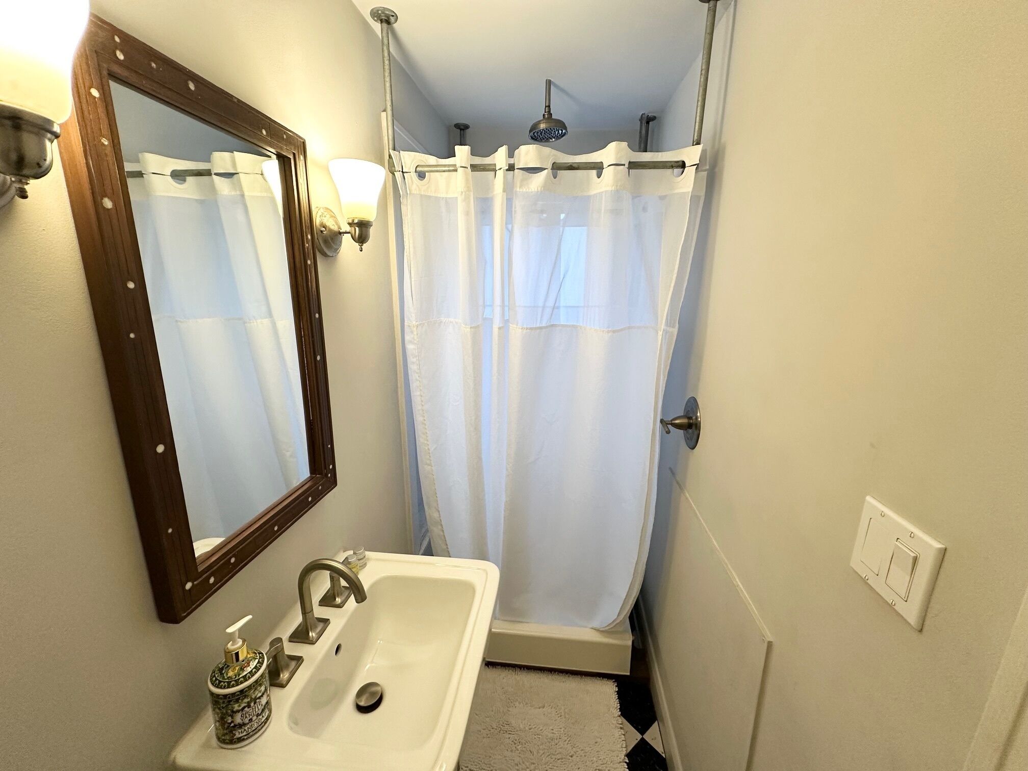 A bathroom with a sink, mirror, shower curtain, and a light fixture.