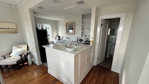 A modern kitchen with white cabinetry, a central island, and a dining area with a chair. - The Vurpillat Beachfront Hotel (Hermosa Beach)