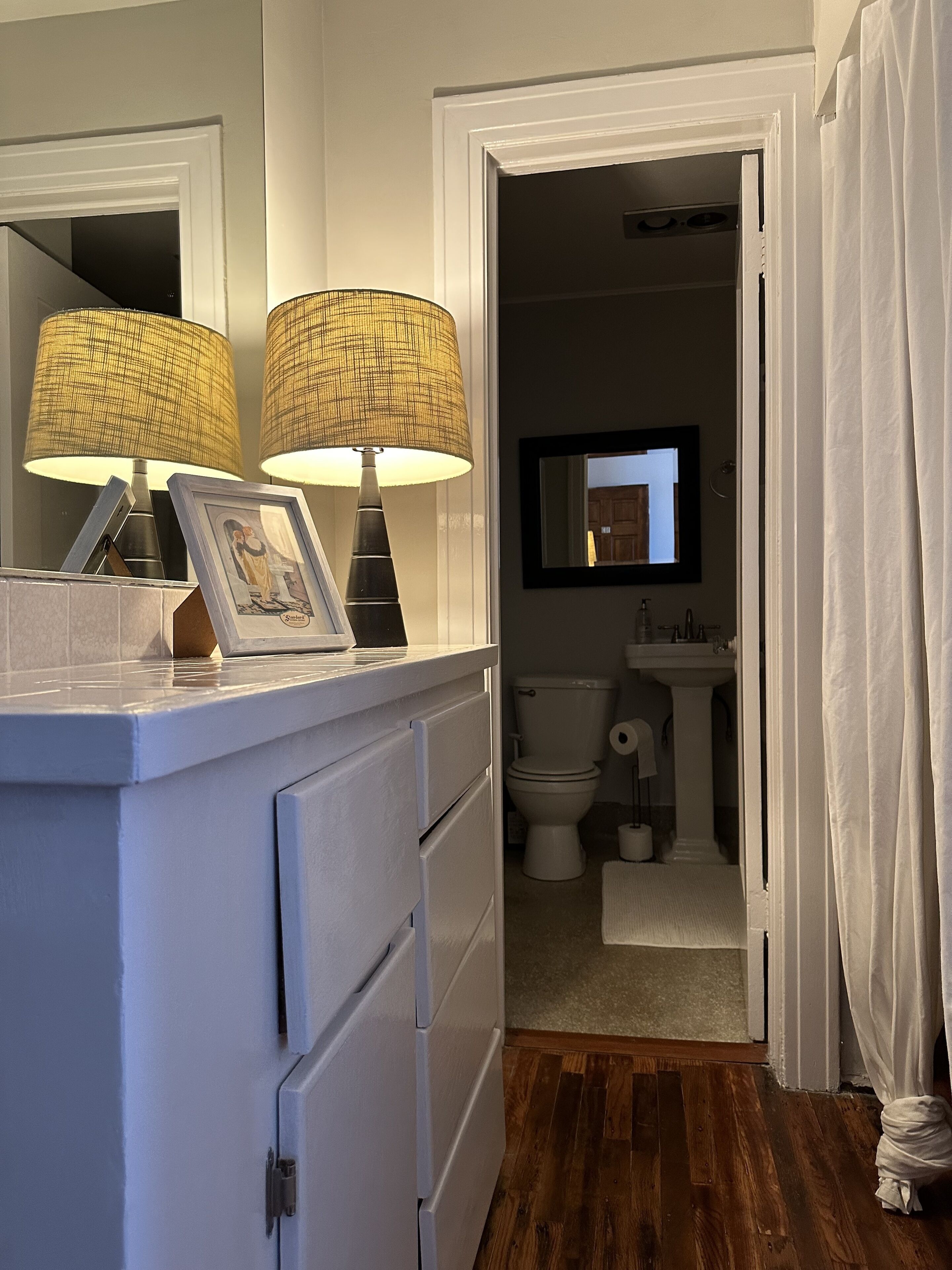 A bathroom with a toilet, sink, and mirror. There are two lamps on the vanity.