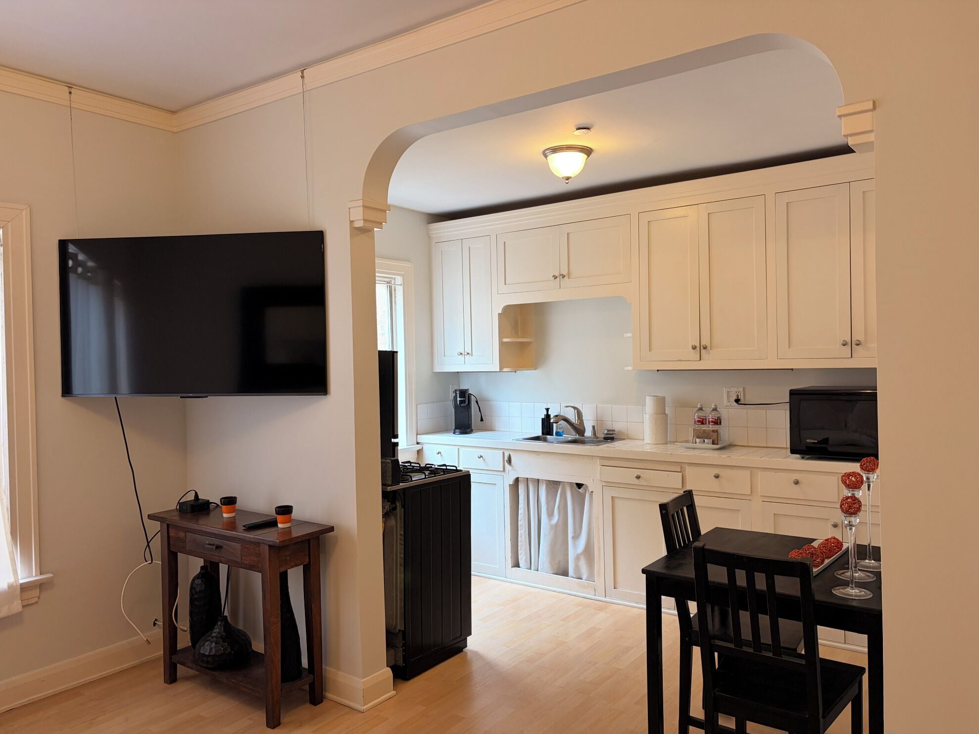 A modern kitchen with white cabinets, a flat-screen TV, a dining table with chairs, and a small table with a coffee machine.