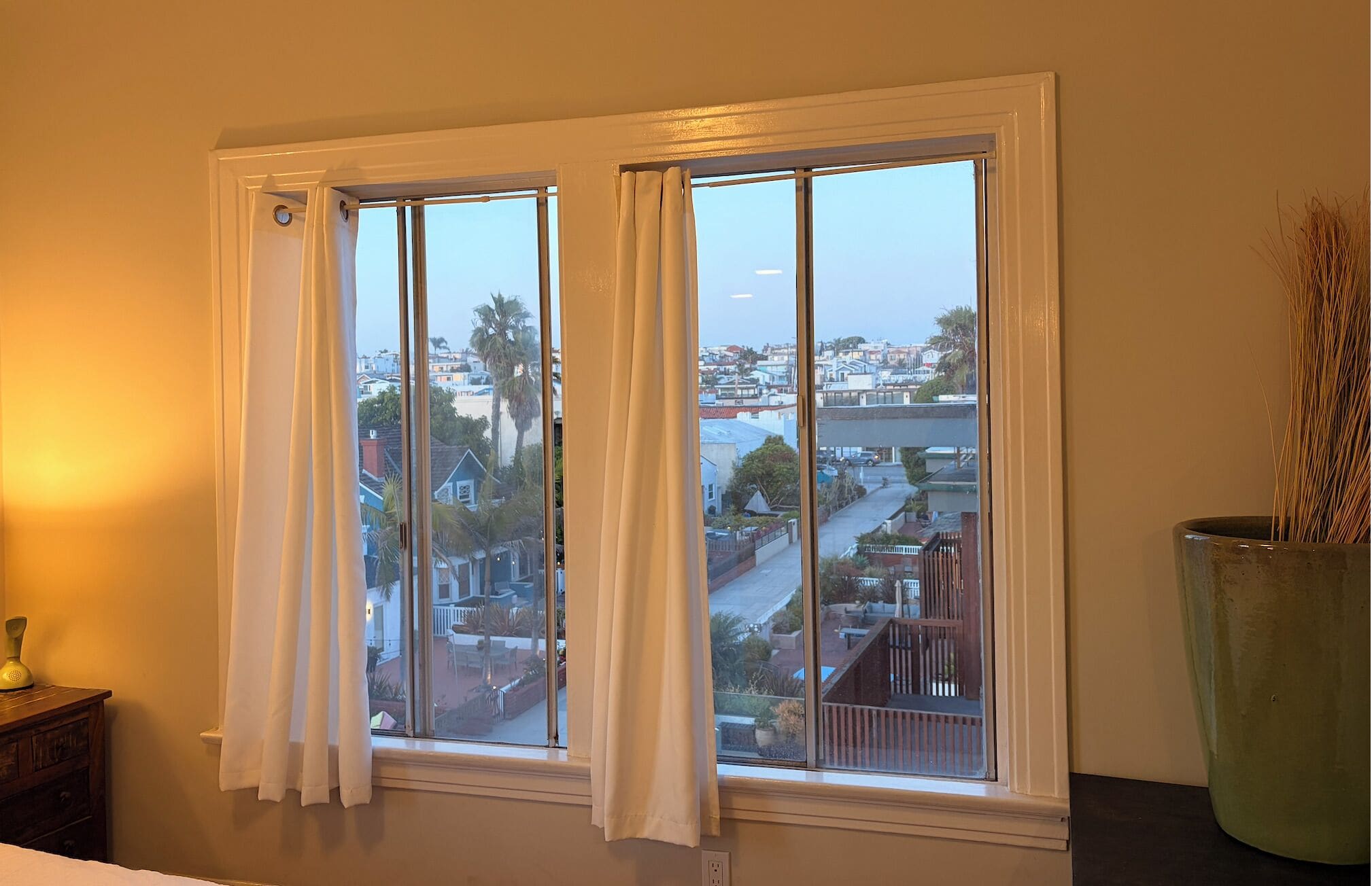 A room with a large window, a potted plant, and a wooden dresser.