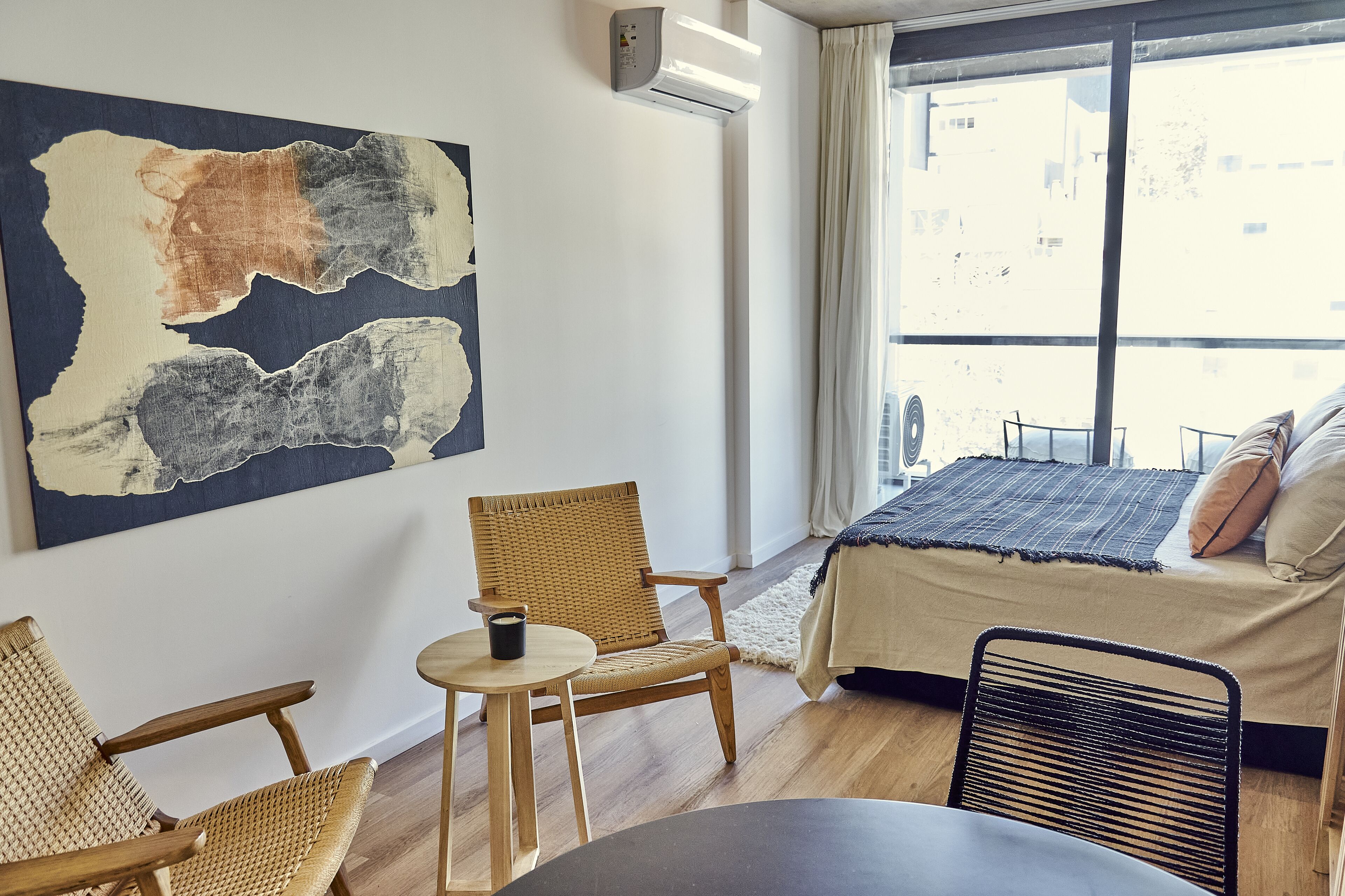 A room with a bed, a chair, a small table, and a large abstract painting on the wall.