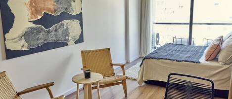 A room with a bed, a chair, a small table, and a large abstract painting on the wall.