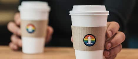 Two disposable coffee cups with a rainbow logo on a wooden table.