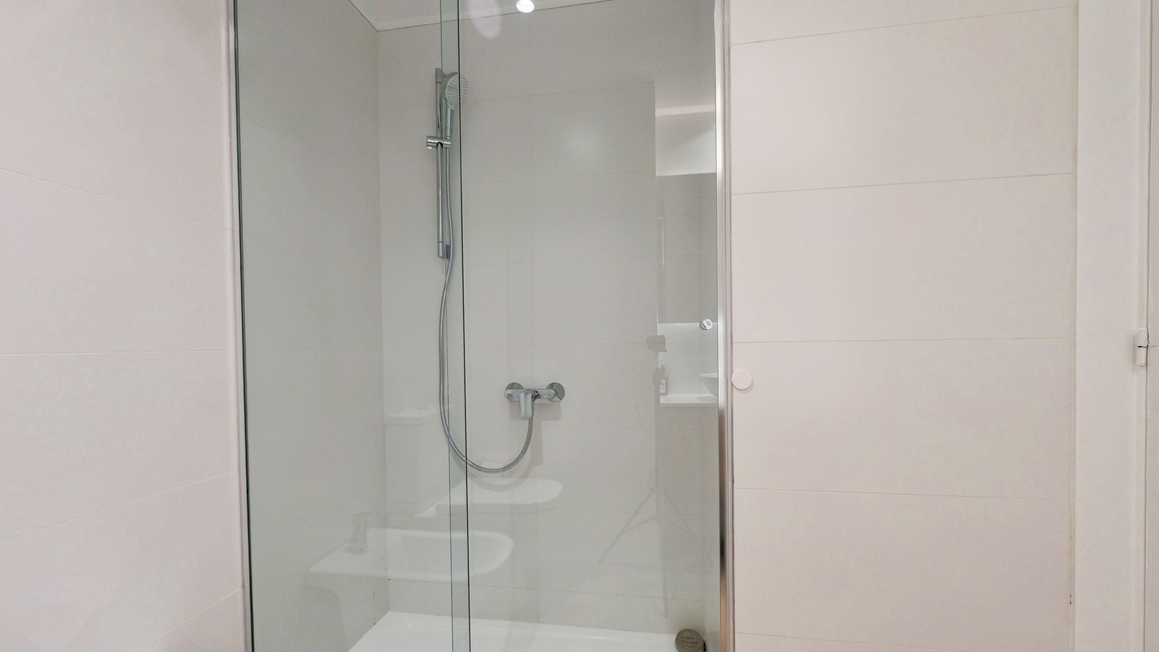 A modern shower with a glass door, a handheld showerhead, and a wall-mounted faucet.