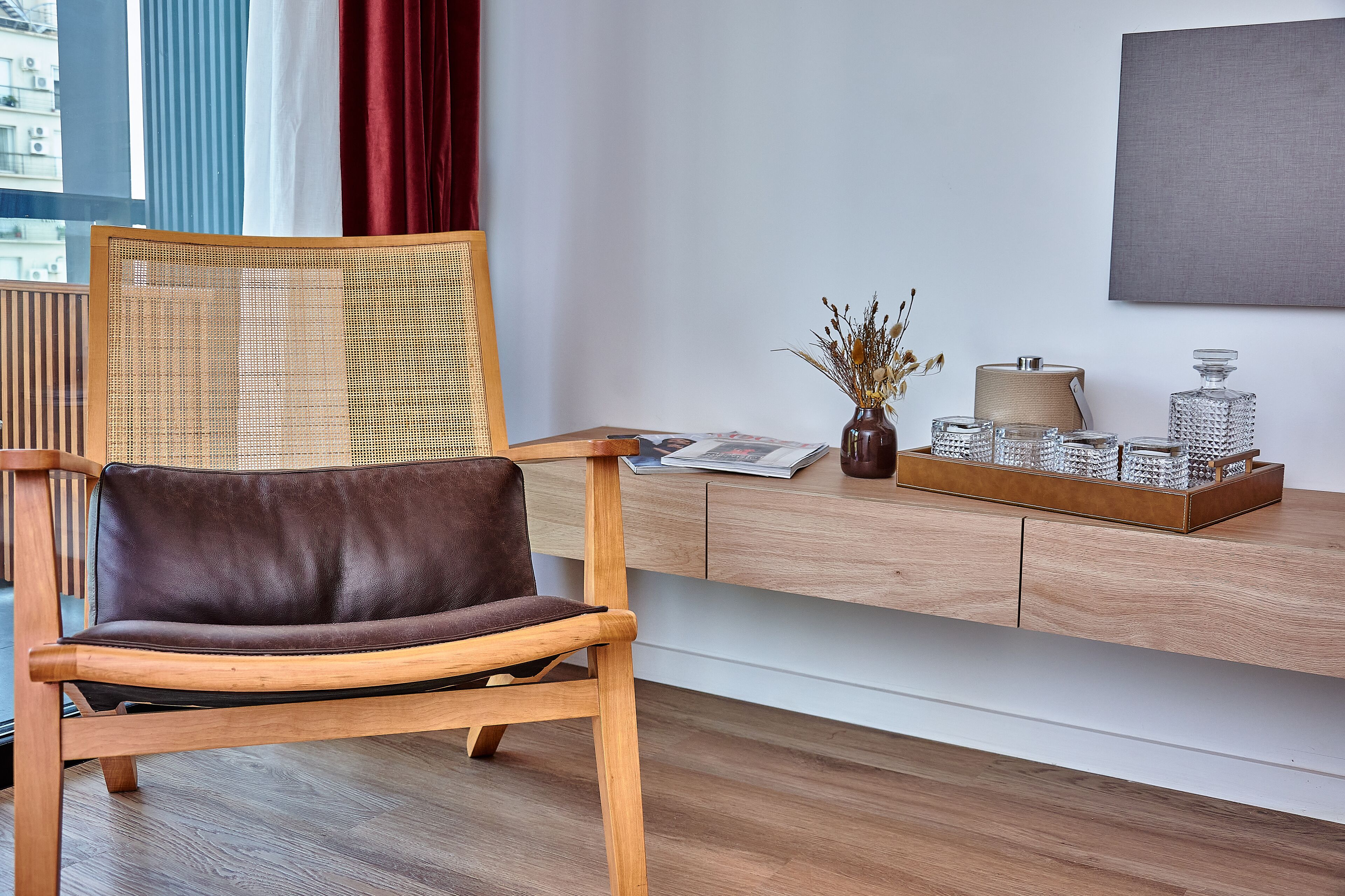 Ein modernes Zimmer mit einem Holzstuhl, einem Holztischchen und Blick auf die Stadt durch große Fenster.