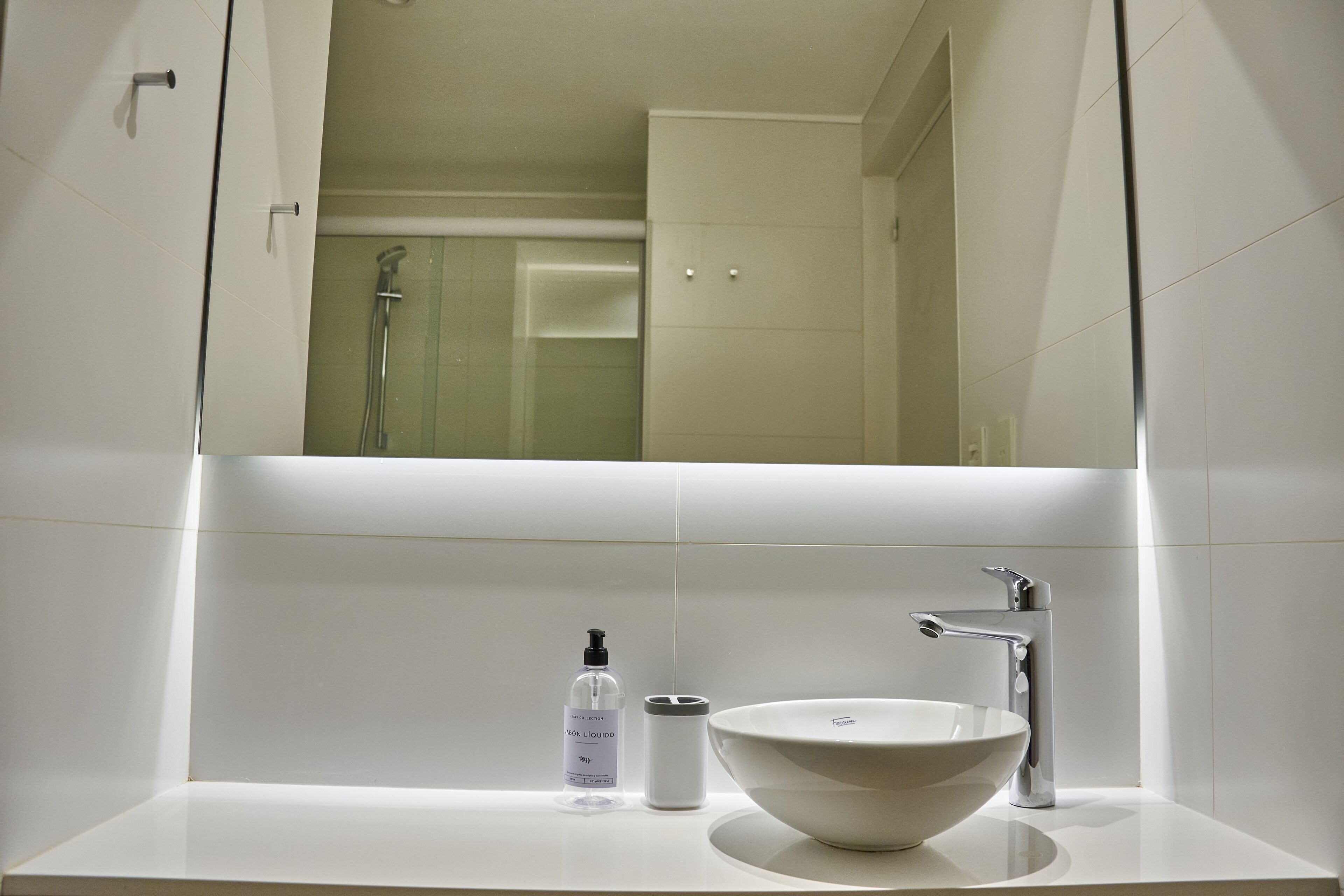 Un baño moderno con lavamanos blanco, espejo y ducha.