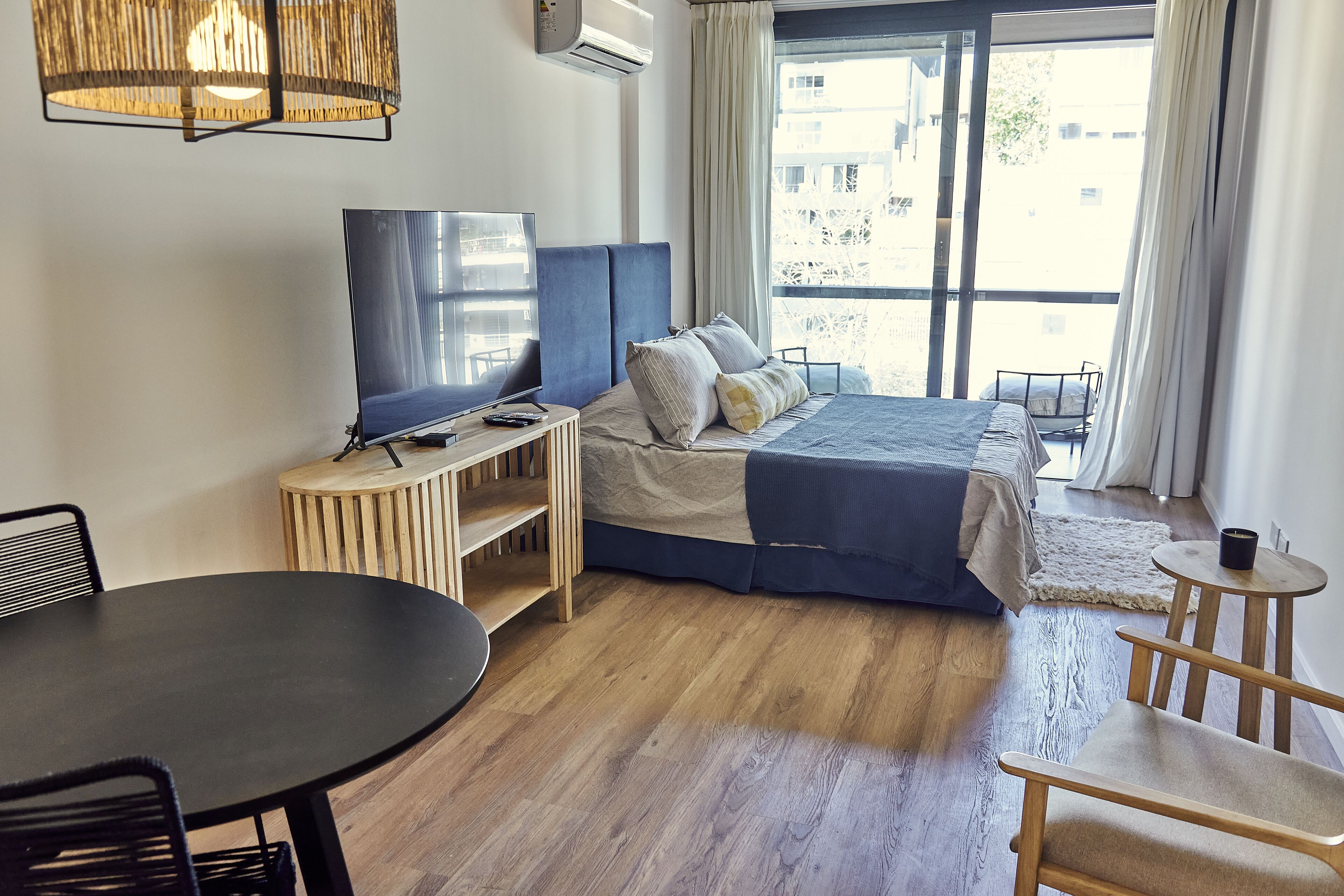 A modern hotel room with a bed, a TV, a dining table, and a small seating area.