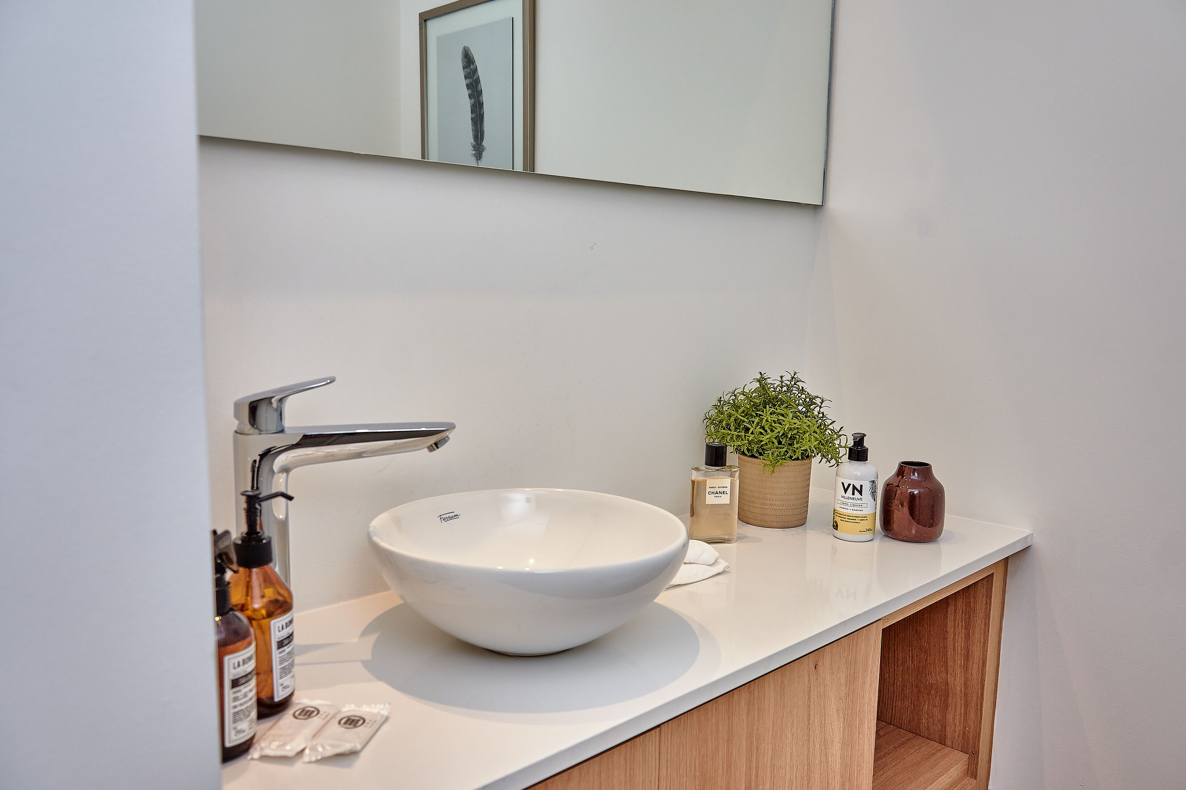Un baño moderno con un lavamanos blanco, un espejo y un mueble de tocador de madera.