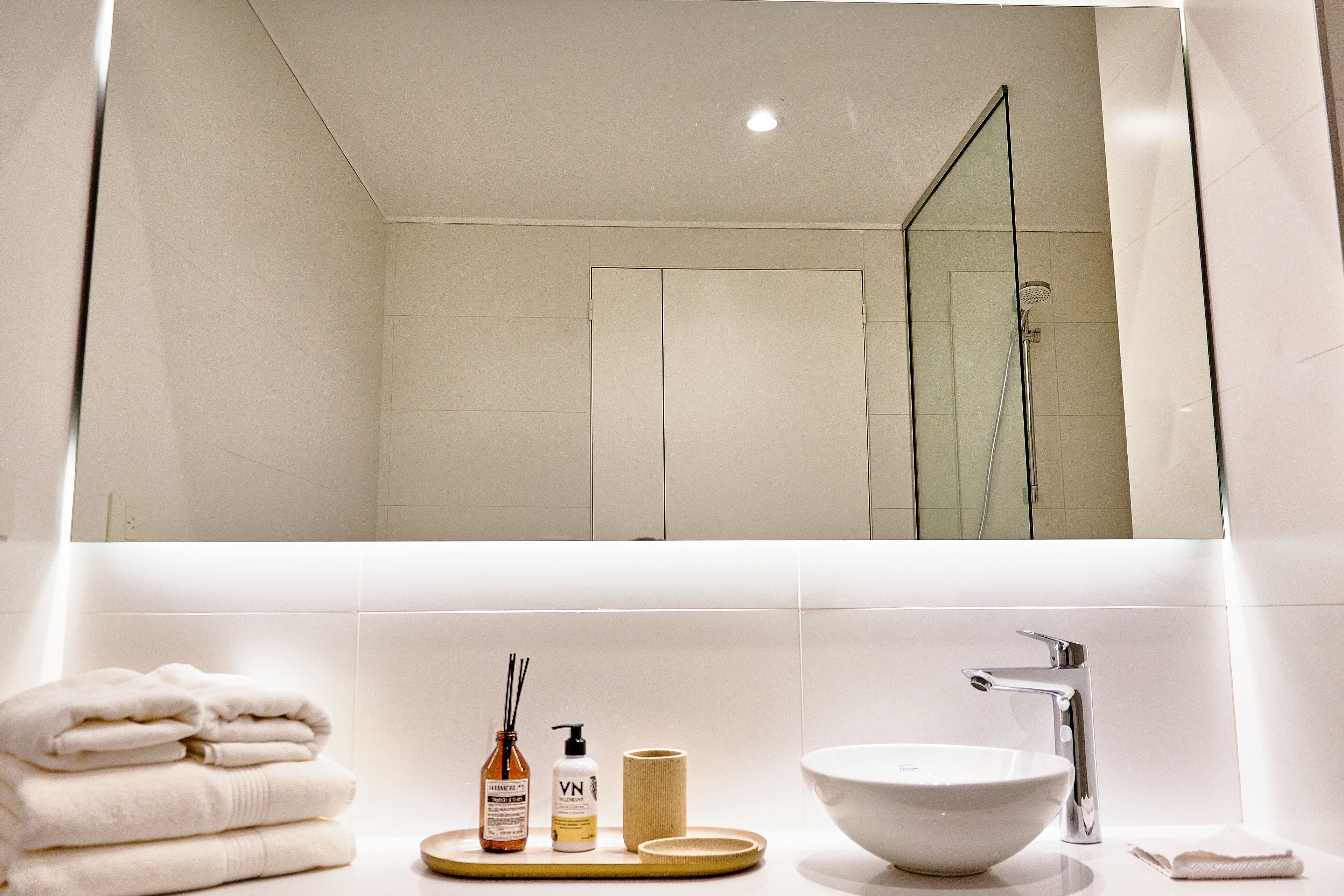 Une salle de bain moderne avec un grand miroir, un lavabo et une douche.