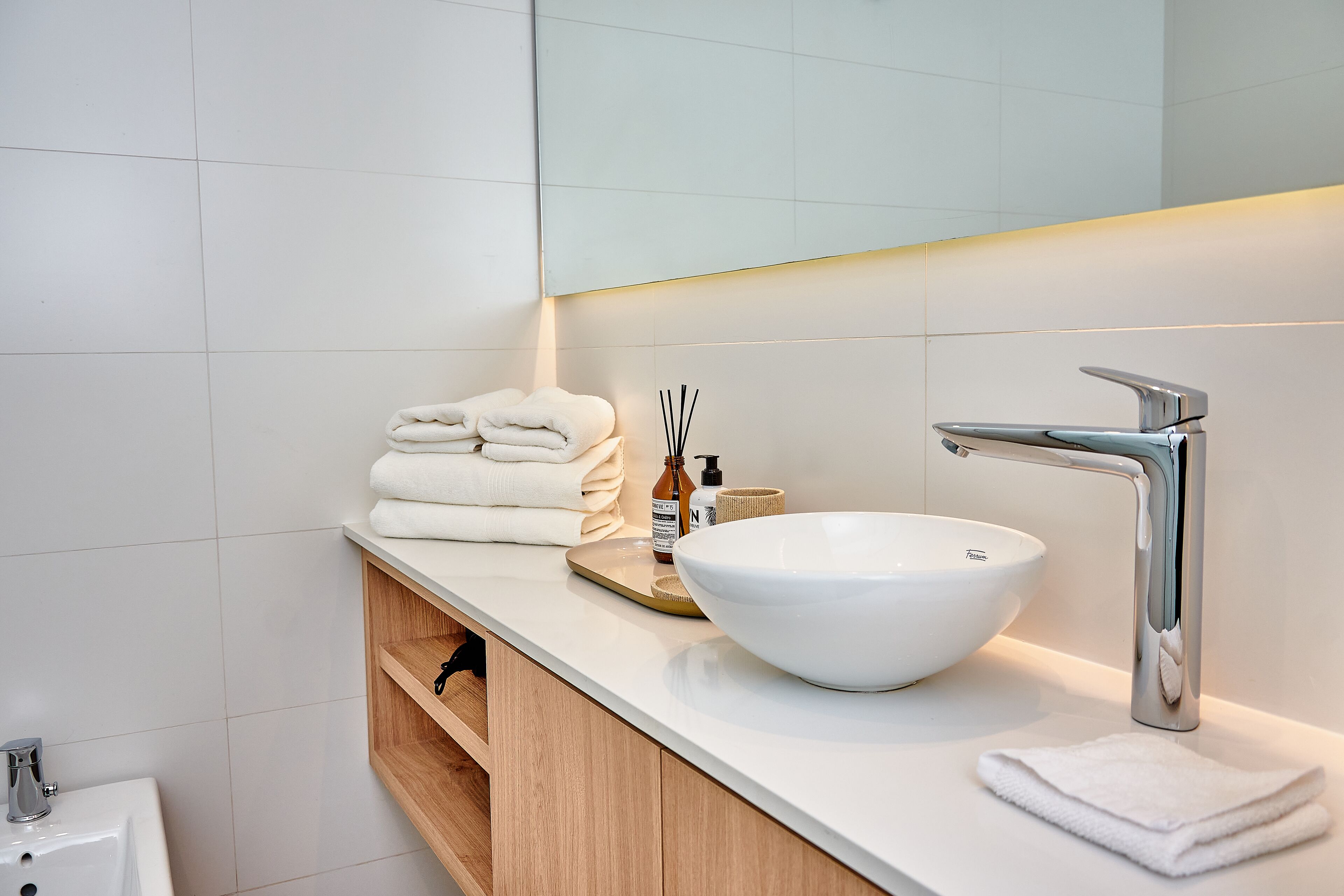 Een moderne badkamer met een wit wastafeltje, een grote spiegel en netjes opgevouwen handdoeken.