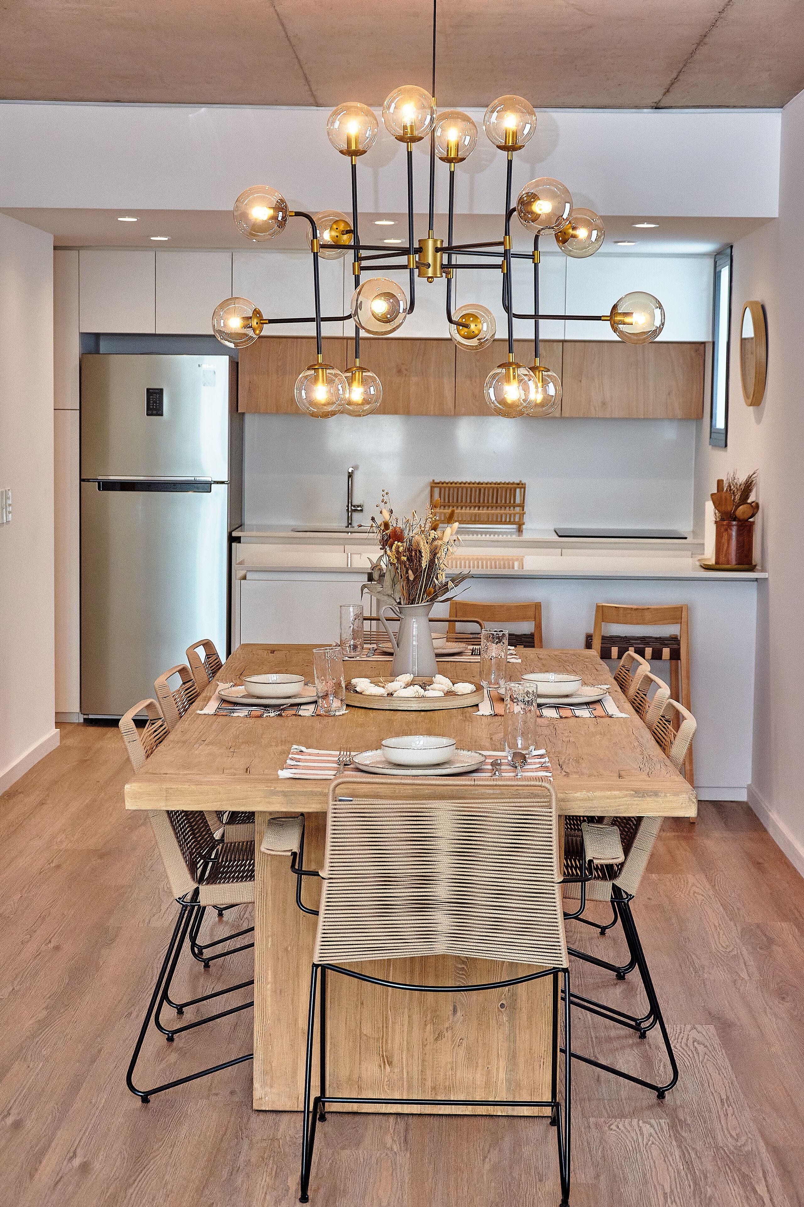 A modern kitchen with a wooden dining table, chairs, and a chandelier.