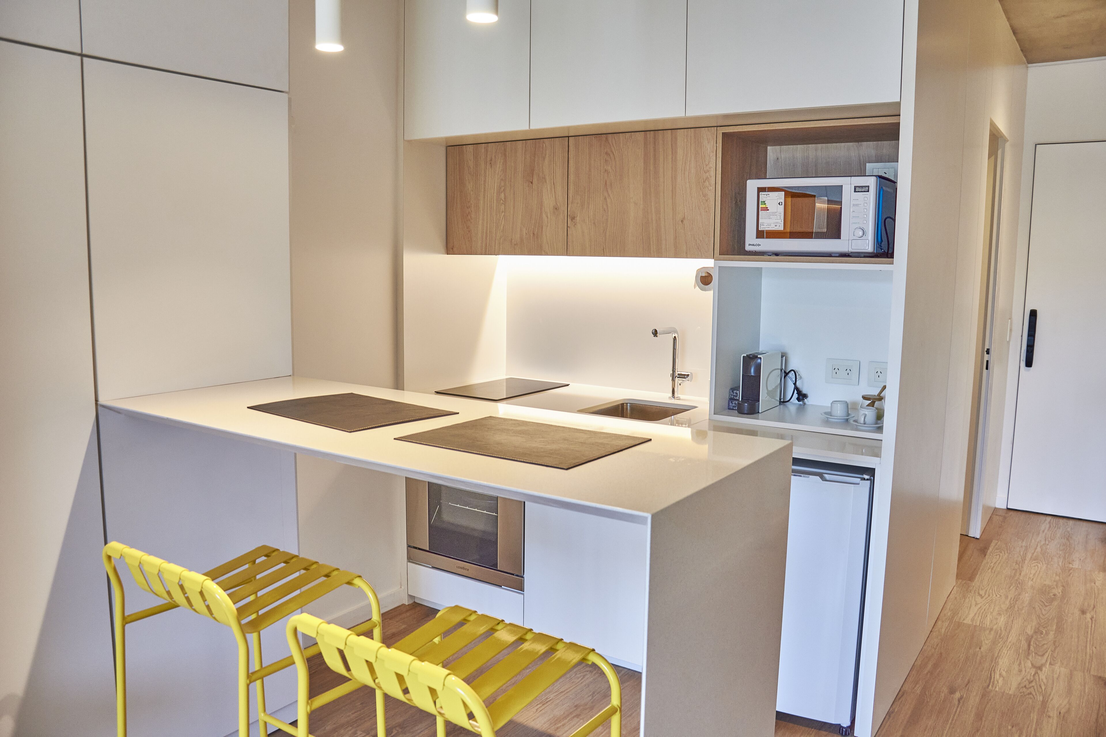 A compact kitchen with a central island, a microwave, and a refrigerator. There are two yellow chairs at the island.