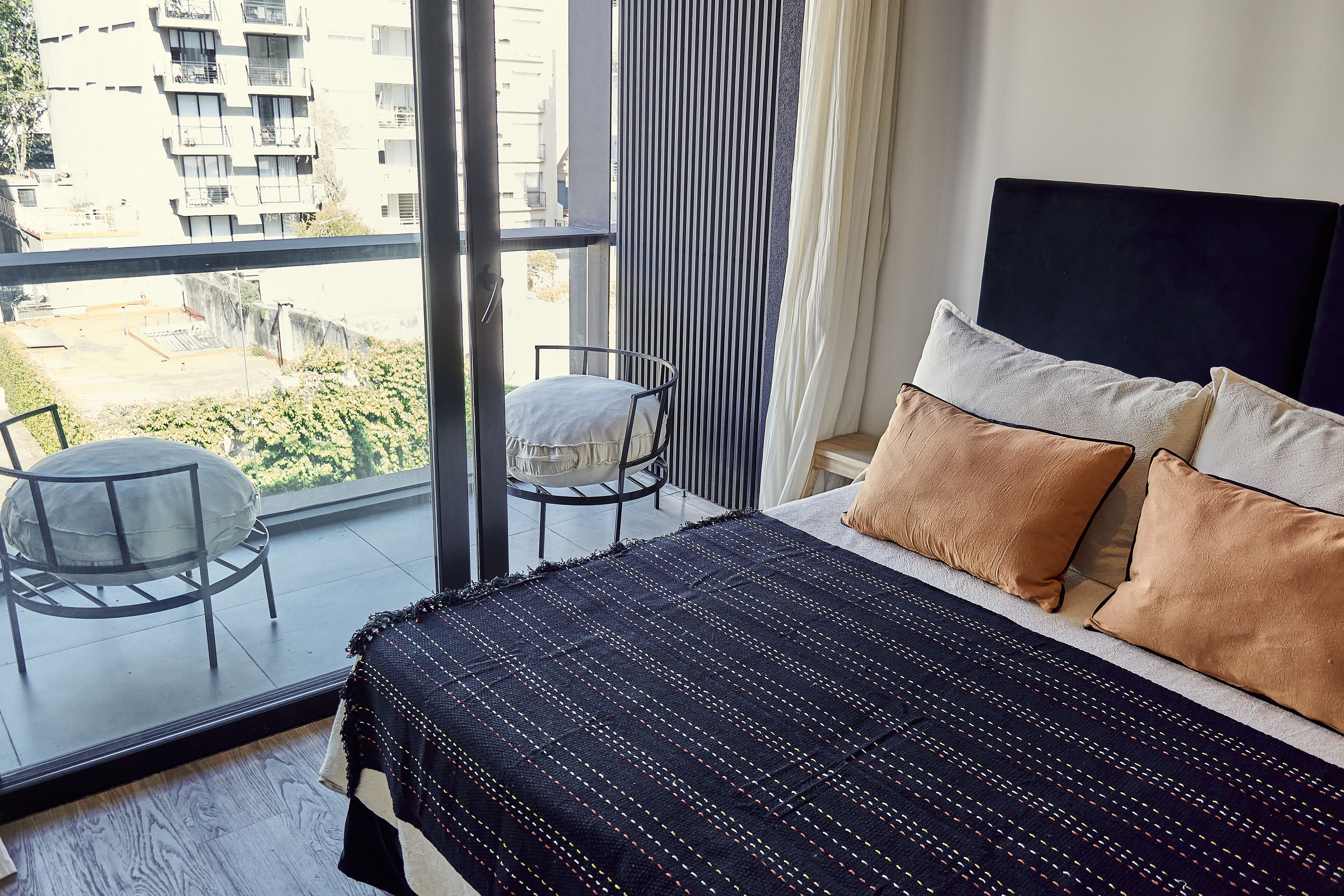 Een slaapkamer met een groot bed, een stoel en uitzicht op de stad vanaf een balkon.