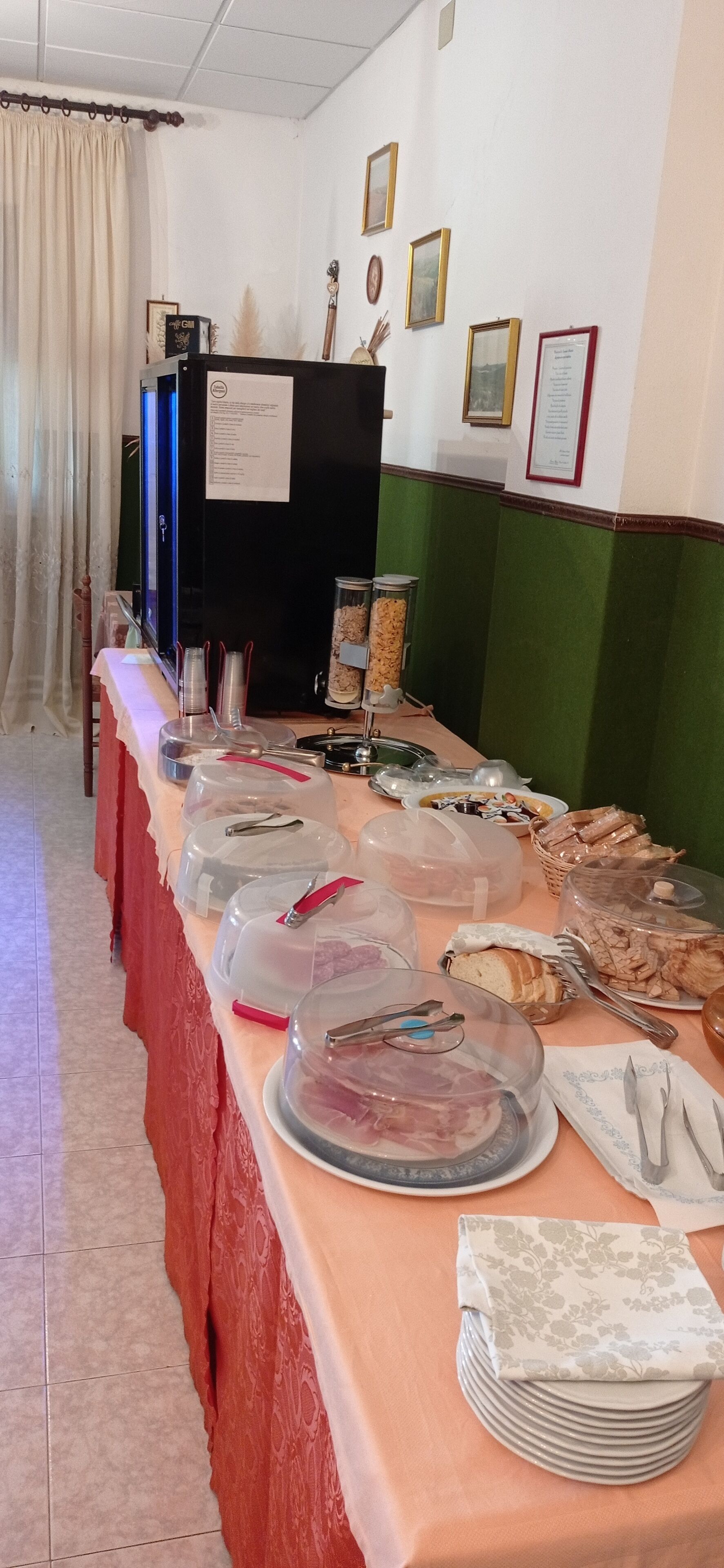 A buffet table with various food items and utensils, a black refrigerator, and framed certificates on the wall.