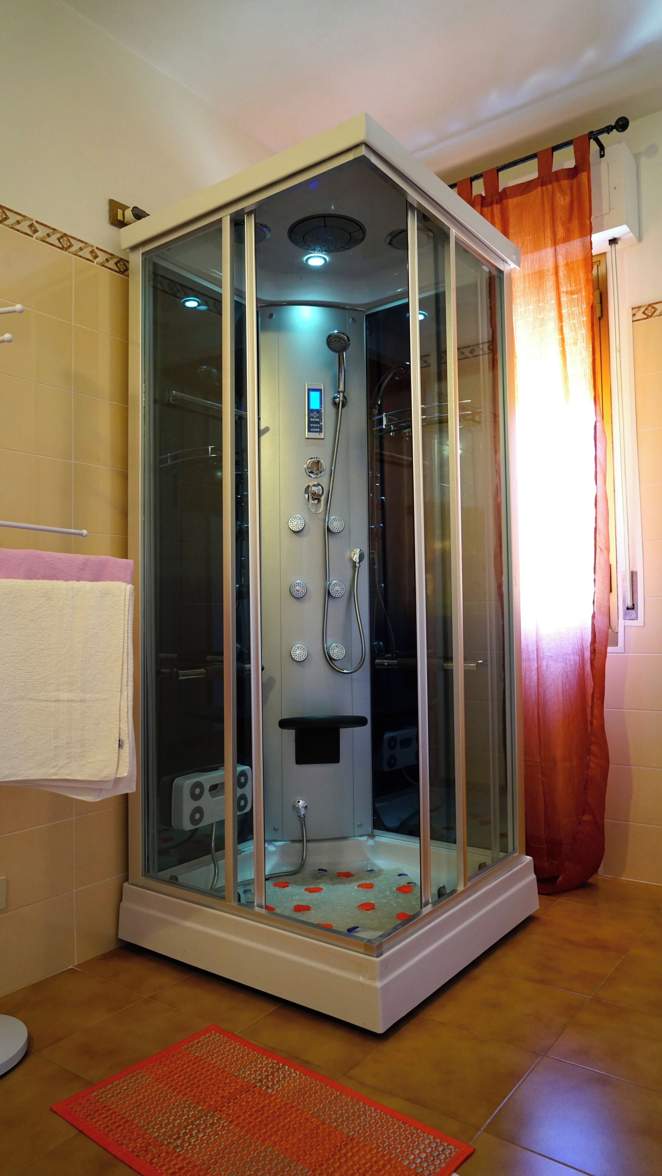 A glass-enclosed shower stall with a control panel, a handheld showerhead, and a handheld shower attachment.