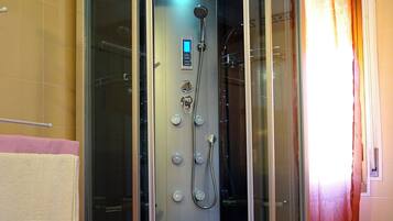 A glass-enclosed shower stall with a control panel, a handheld showerhead, and a handheld shower attachment.