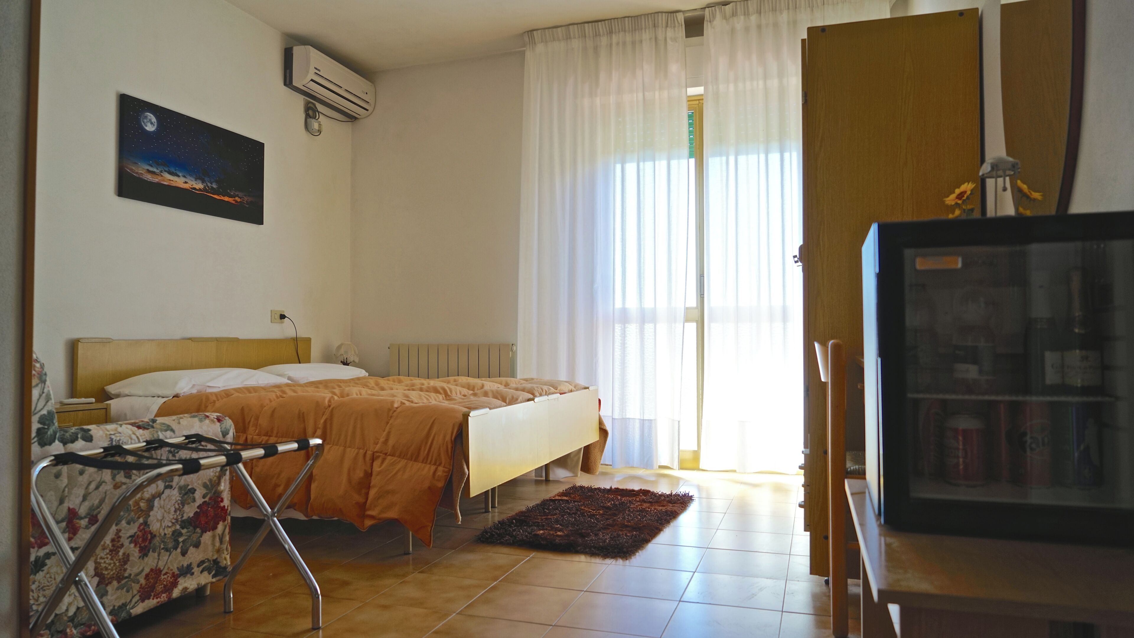 Quarto de hotel com cama, cadeira, televisão e janela com cortinas.