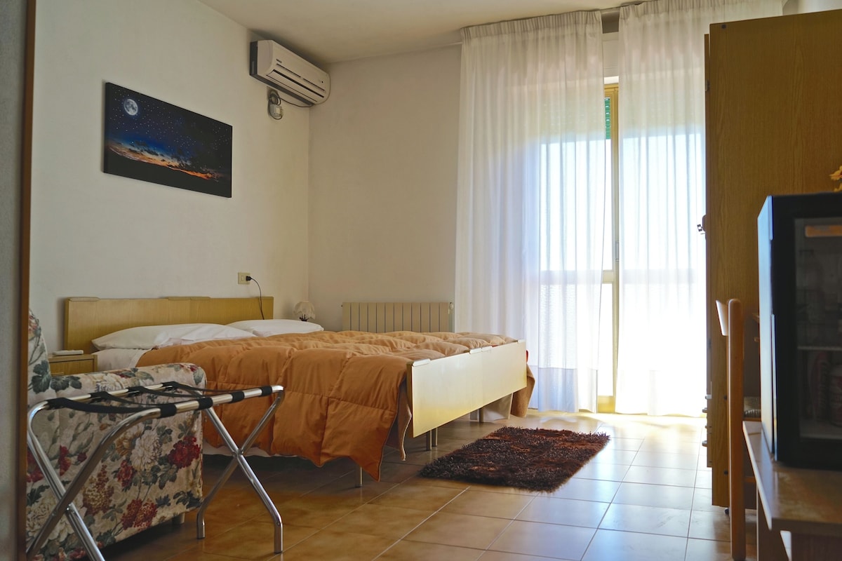 A hotel room with a bed, a chair, a TV, and a window with curtains.