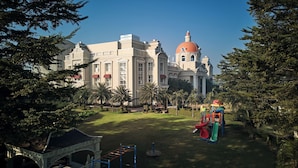 Un grand bâtiment doté d’un dôme imposant et d’une architecture classique, entouré d’un jardin bien entretenu, agrémenté de palmiers et d’une aire de jeux.