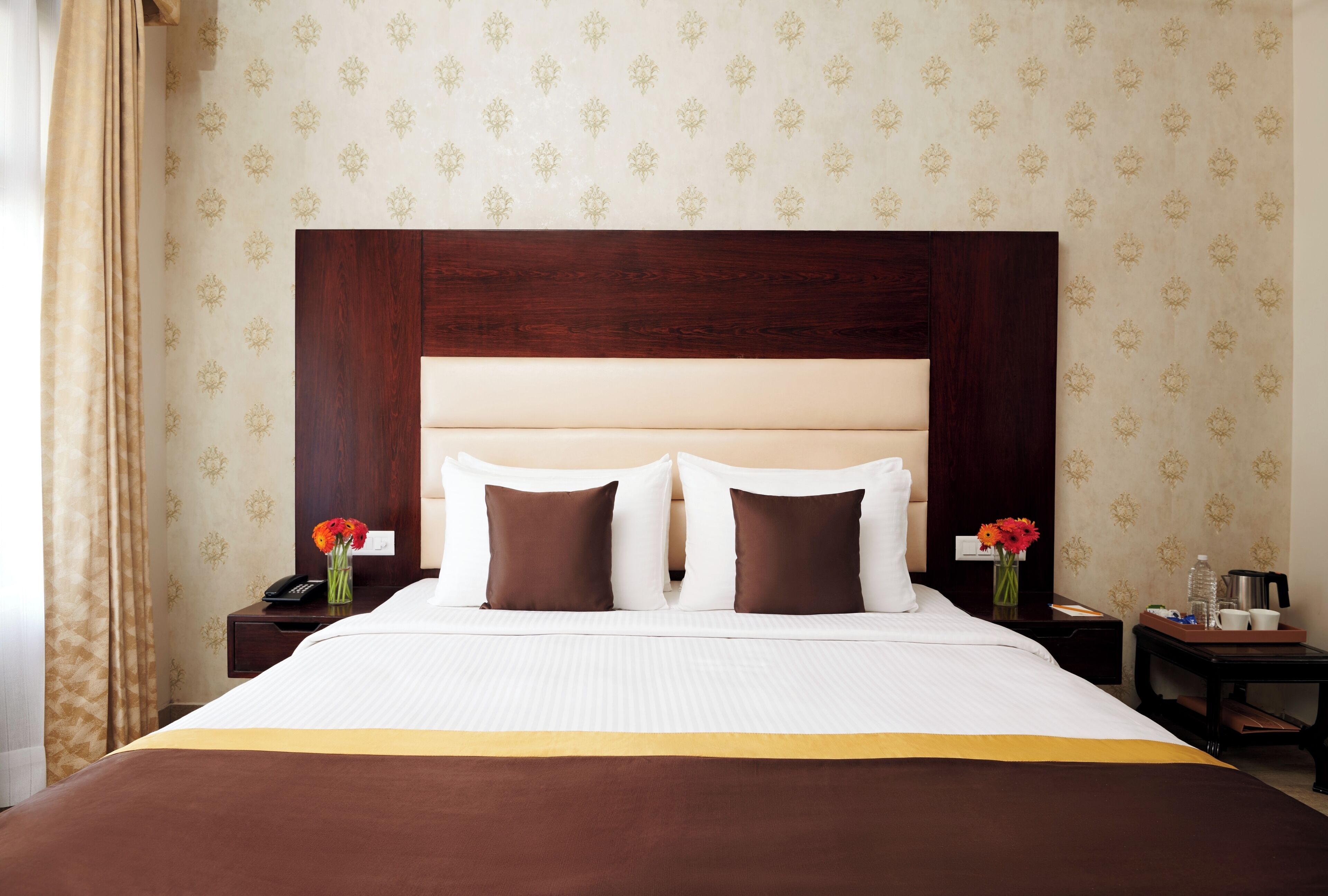 A hotel room with a large bed, two nightstands, a wooden headboard, and floral wallpaper.