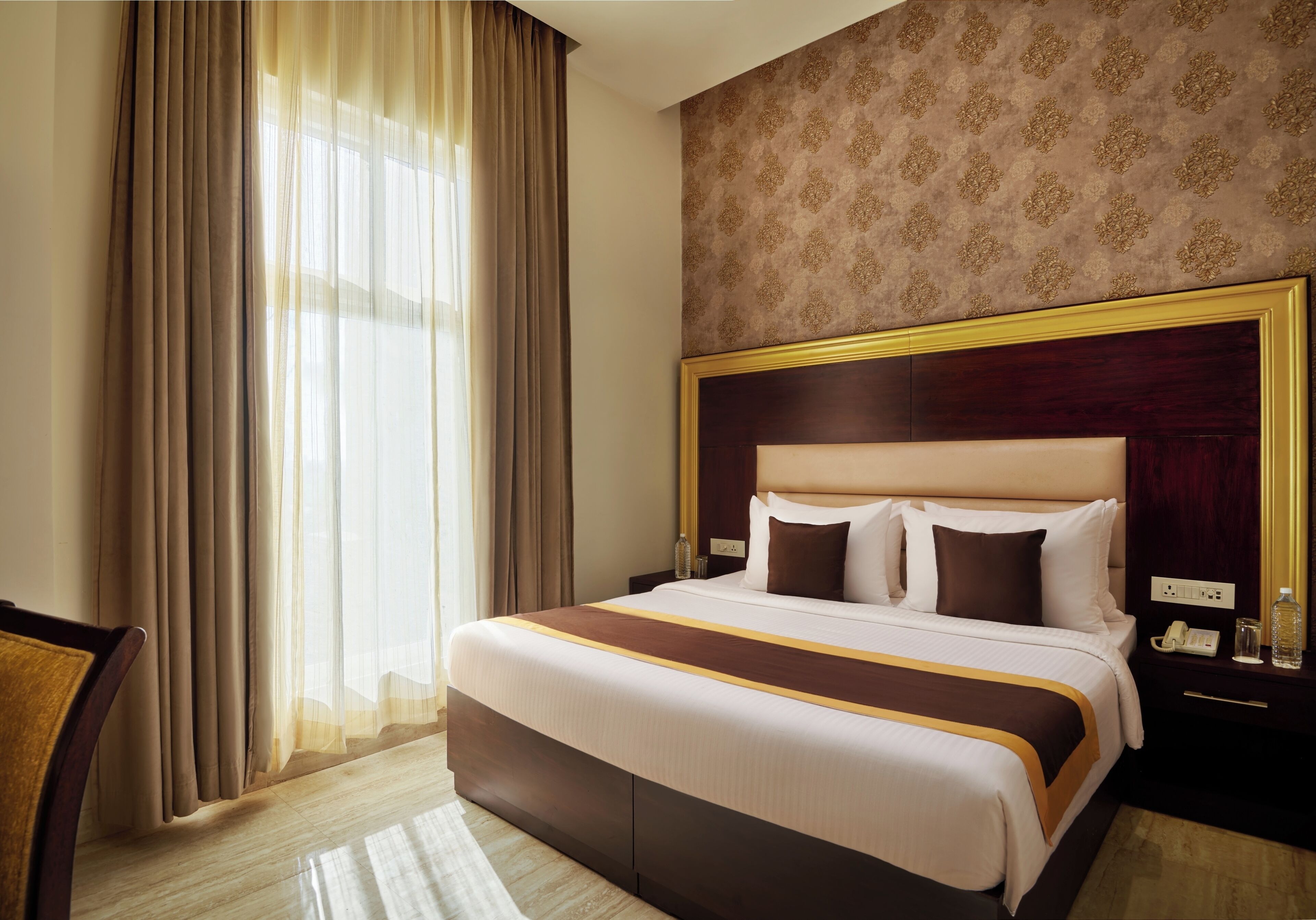 A hotel room with a large bed, a nightstand, a chair, and a window with curtains.