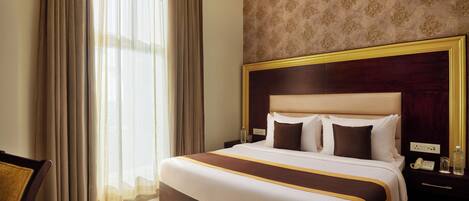 A hotel room with a large bed, a nightstand, a chair, and a window with curtains.