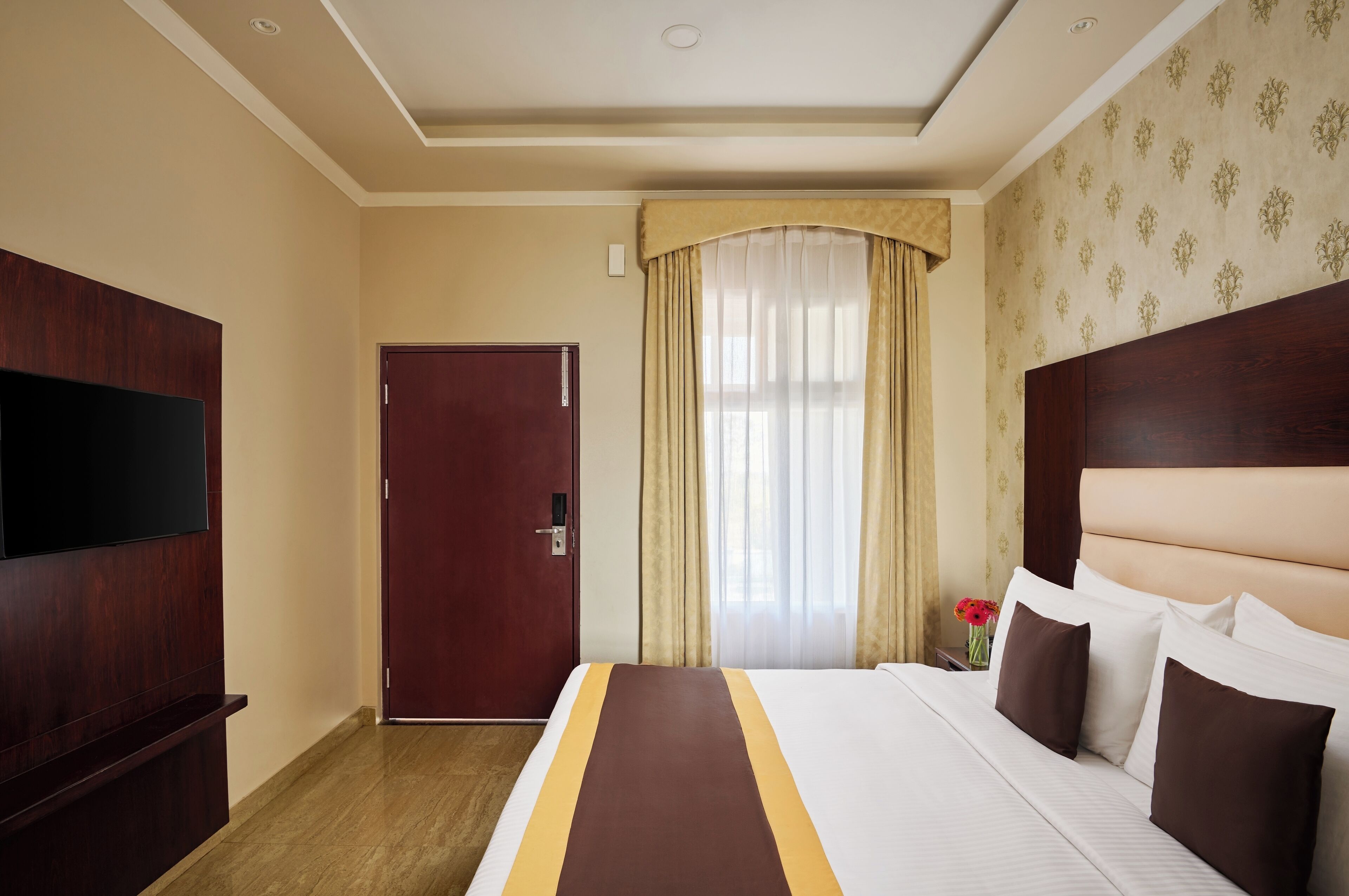 A hotel room with a large bed, a flat-screen TV, a wooden wardrobe, and a door.