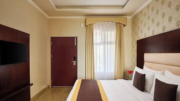 Habitación de hotel con una cama grande, un televisor de pantalla plana, un armario de madera y una puerta.
