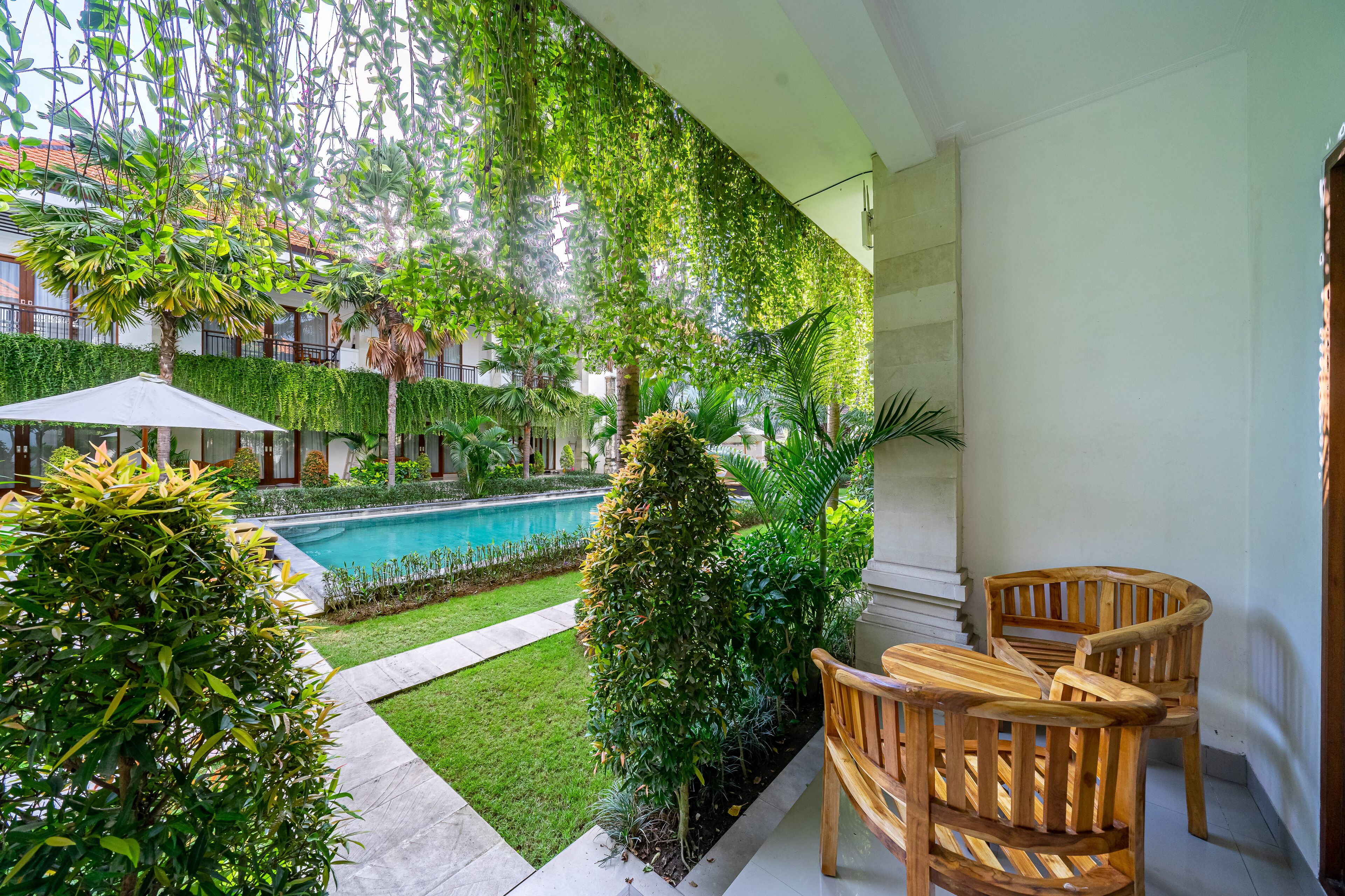 A balcony with a pool, wooden chairs, and lush greenery.